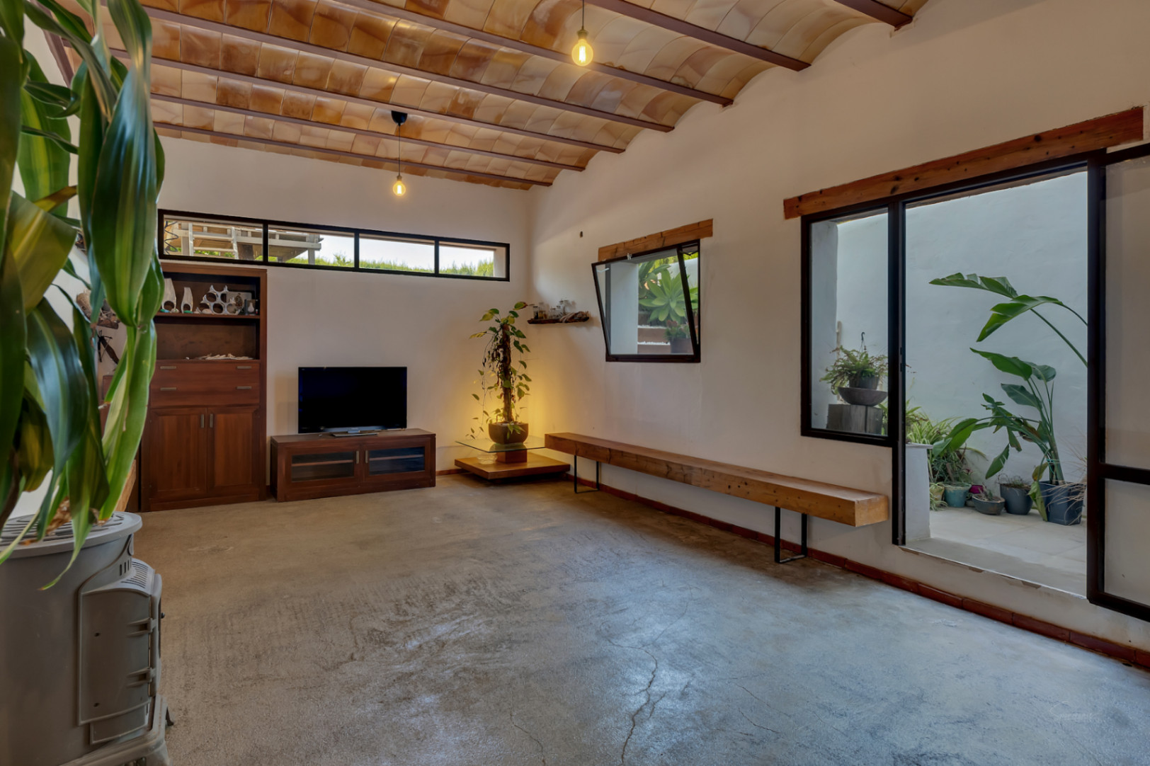 Espace de vie polyvalent en sous-sol avec plafond voûté en terre cuite, sol en béton ciré et accès à un patio intérieur agrémenté de plantes.
