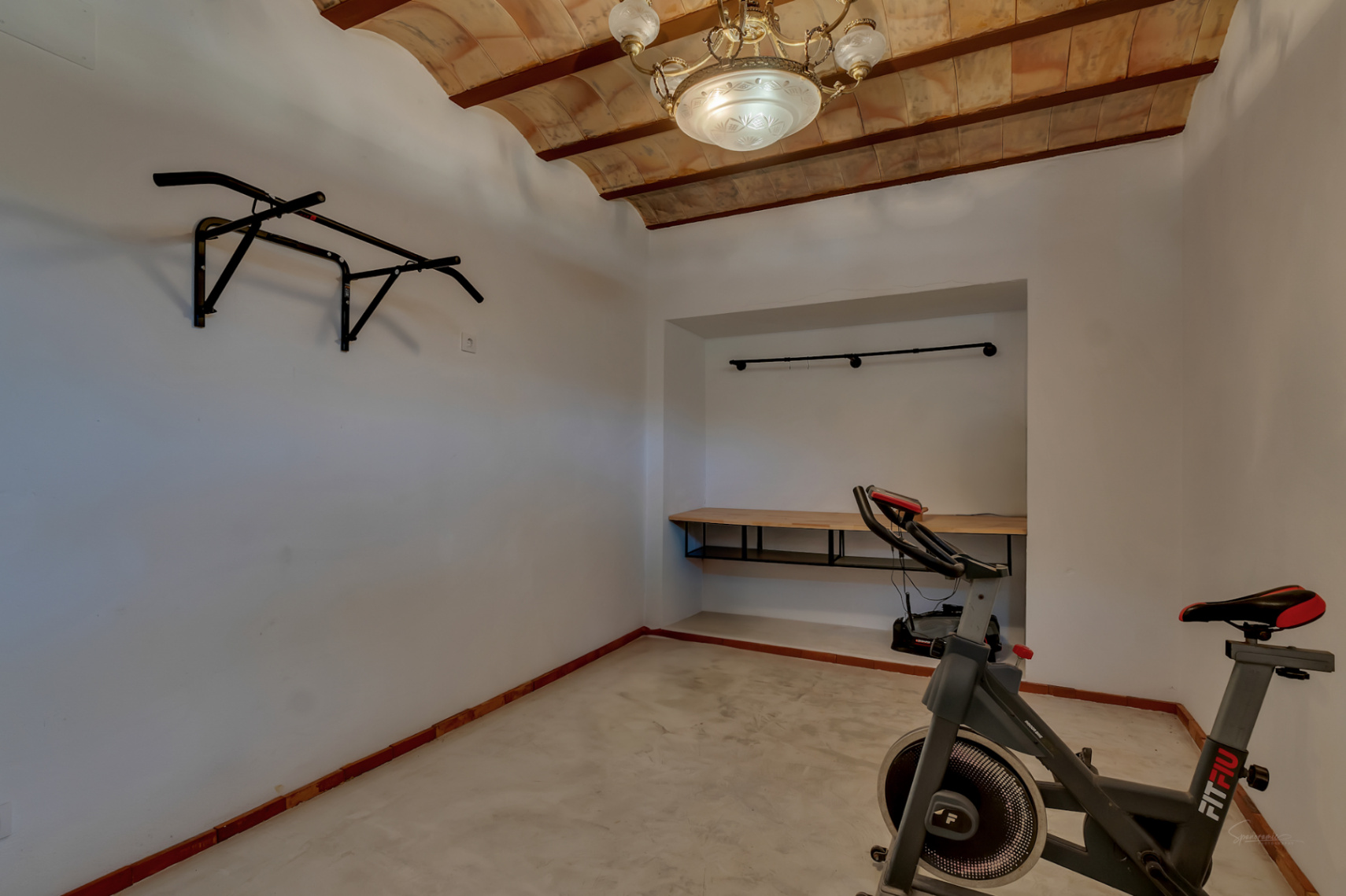 Espace fitness polyvalent avec plafonds voûtés en terre cuite et poutres en bois. Équipé d'un vélo d'appartement, d'une barre de traction et d'un établi intégré.