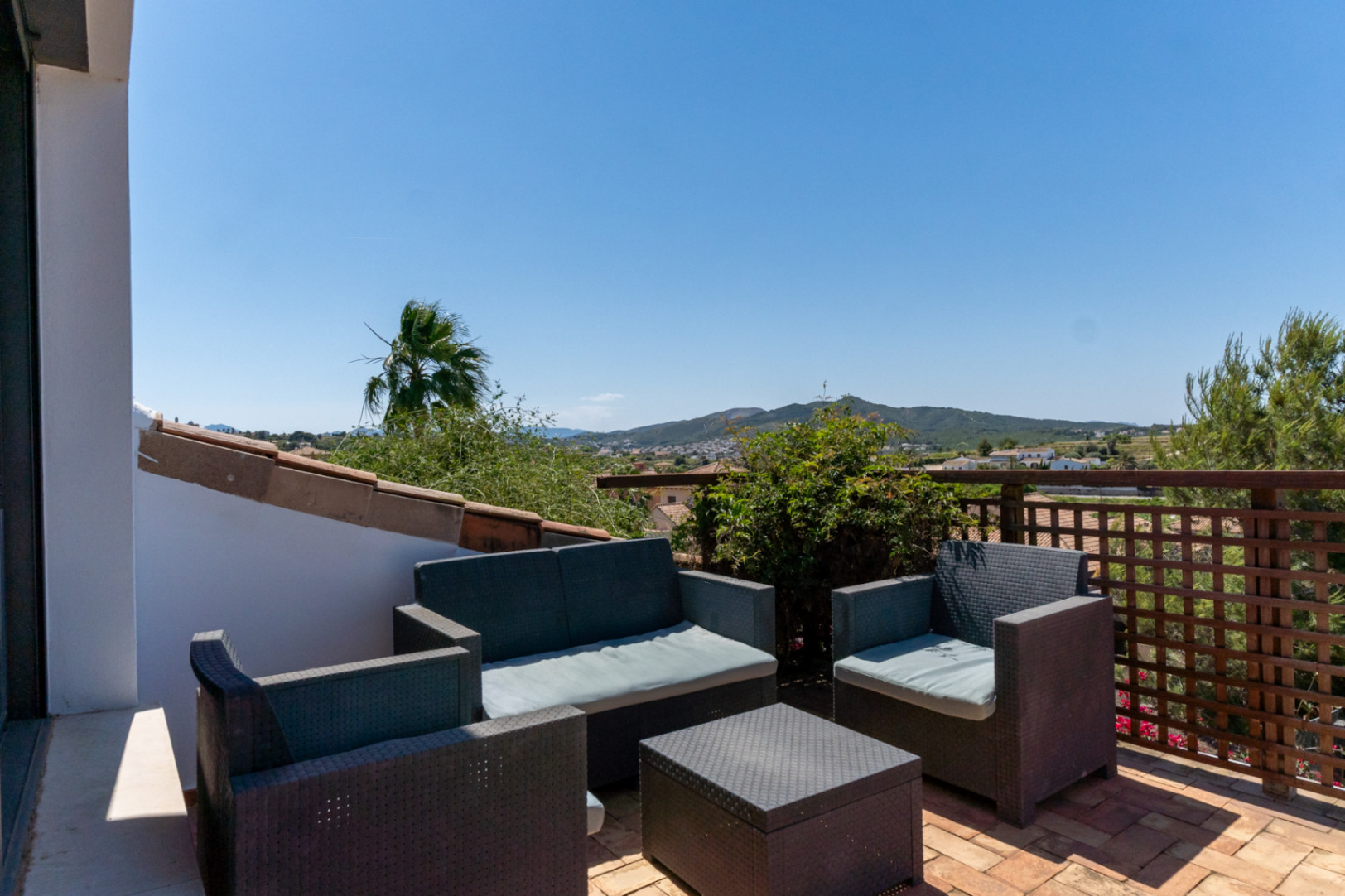 Terrasse supérieure avec salon de jardin en résine tressée et sol en terre cuite, offrant une vue panoramique sur la vallée et les montagnes.