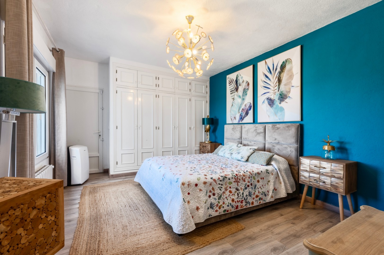 Chambre avec mur d'accent bleu canard, placards intégrés blancs, parquet au sol et un lustre doré moderne créant une atmosphère élégante et lumineuse.
