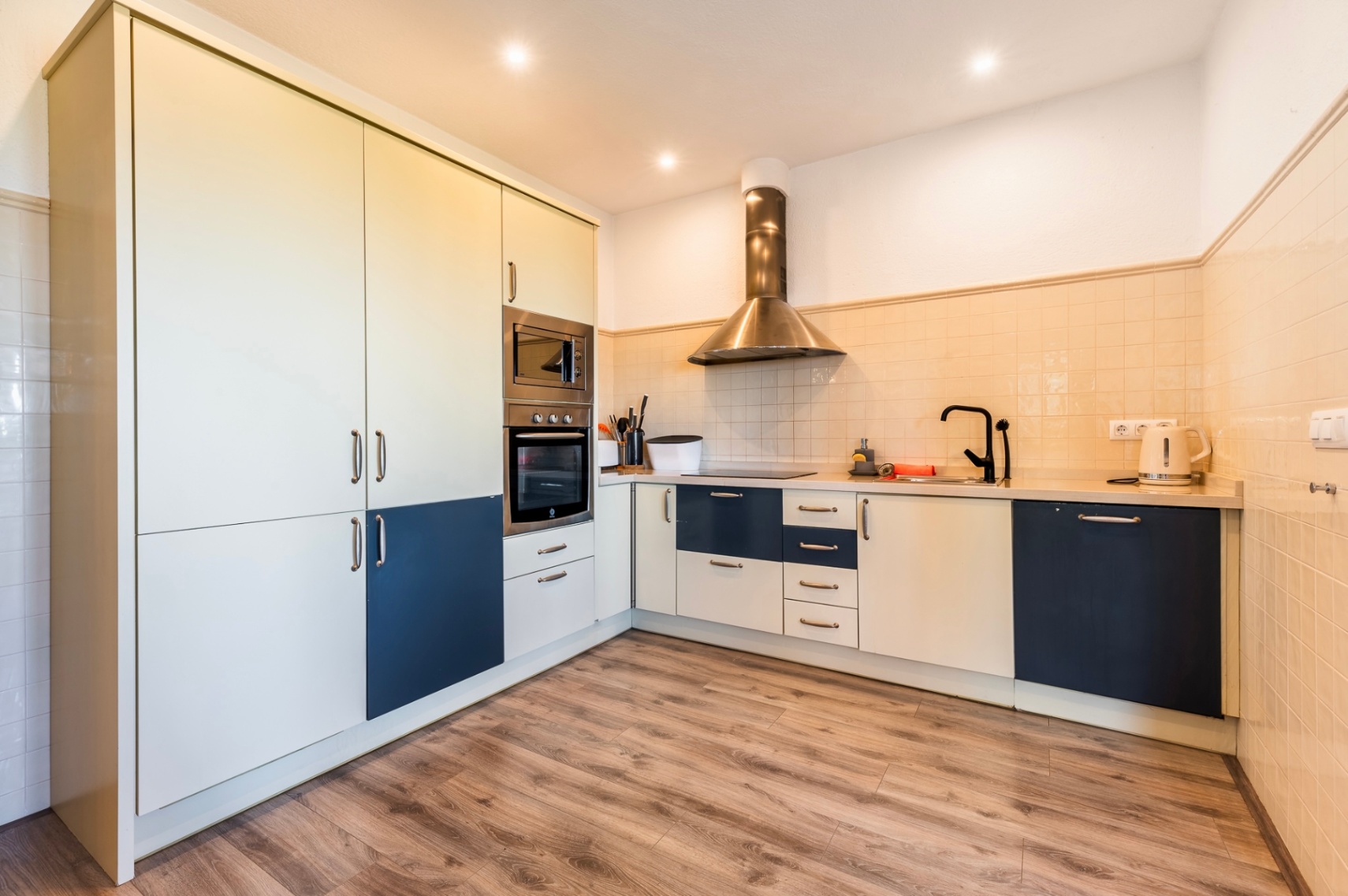 Cuisine moderne rénovée avec placards bicolores bleu et crème, électroménager en acier inoxydable et sol en stratifié aspect bois.