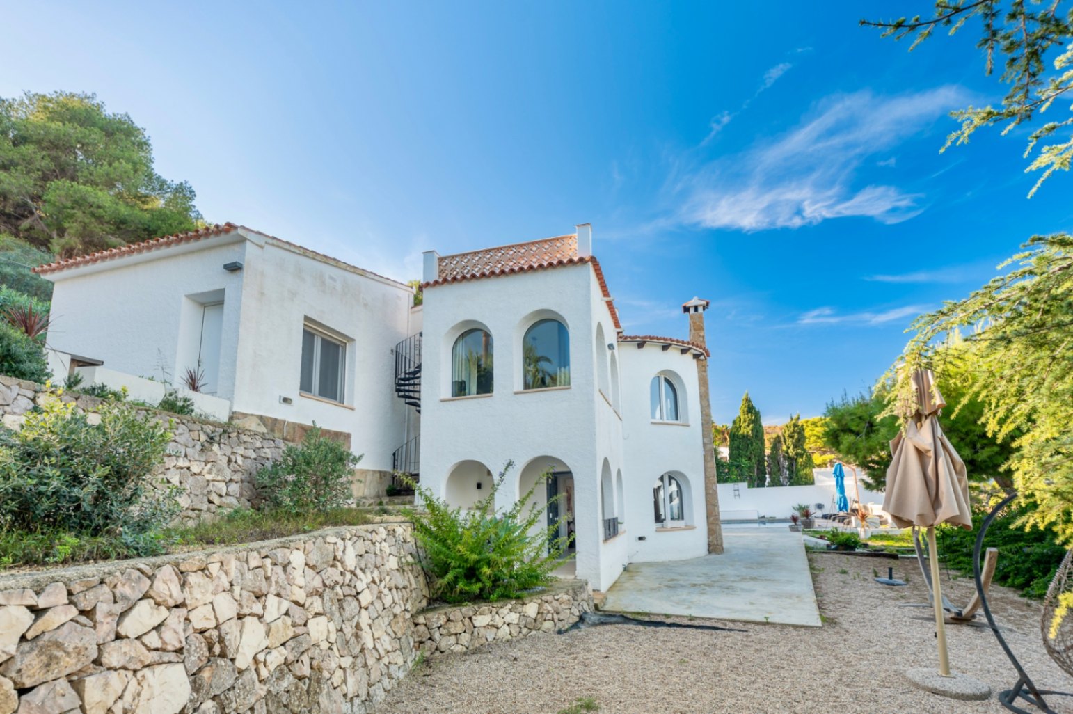 Façade blanche de style méditerranéen avec arches traditionnelles, murs de soutènement en pierre naturelle et escalier en colimaçon extérieur à Jávea.