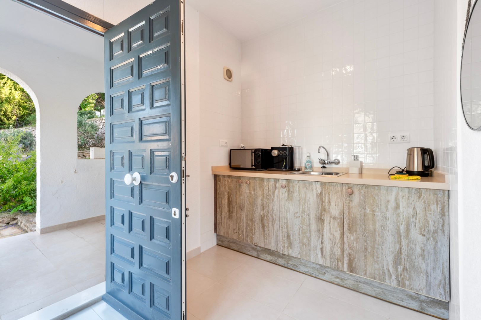Kitchenette compacte avec des meubles effet bois rustique et un plan de travail clair, située à côté d'une porte à panneaux bleue ouvrant sur l'extérieur.