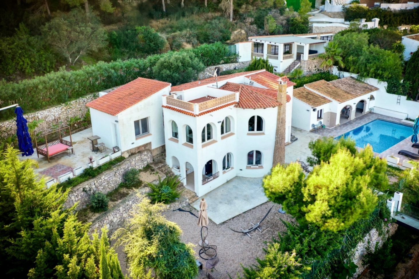 Vue aérienne de la villa méditerranéenne avec façades blanches et toits en tuiles. La propriété dispose d'une piscine, d'une cuisine d'été et de terrasses avec murs en pierre.