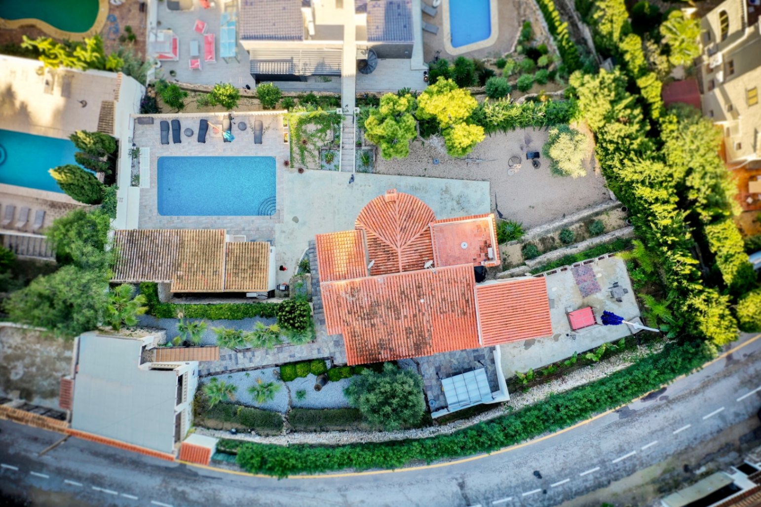 Vue aérienne de la villa soulignant le toit en tuiles rouges, la piscine rectangulaire avec sa terrasse et l'aménagement du terrain paysager à Portitxol.