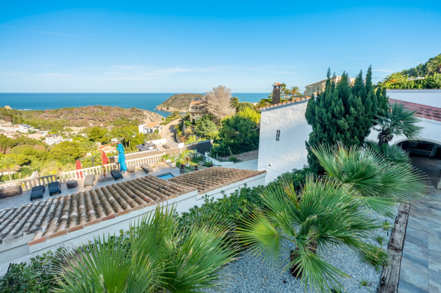 Vue panoramique depuis la propriété sur la mer Méditerranée, mettant en valeur les toits en tuiles traditionnelles et le jardin méditerranéen.