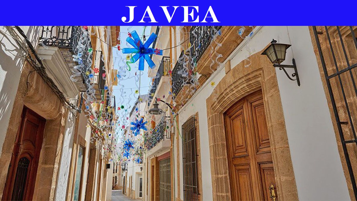 Rue traditionnelle de la vieille ville de Jávea avec des façades blanches, des encadrements en pierre Tosca et des décorations festives.