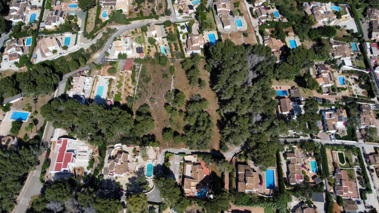 Vue aérienne de la grande parcelle plane, arborée de pins et située au cœur d'un quartier résidentiel calme composé de villas avec piscines.