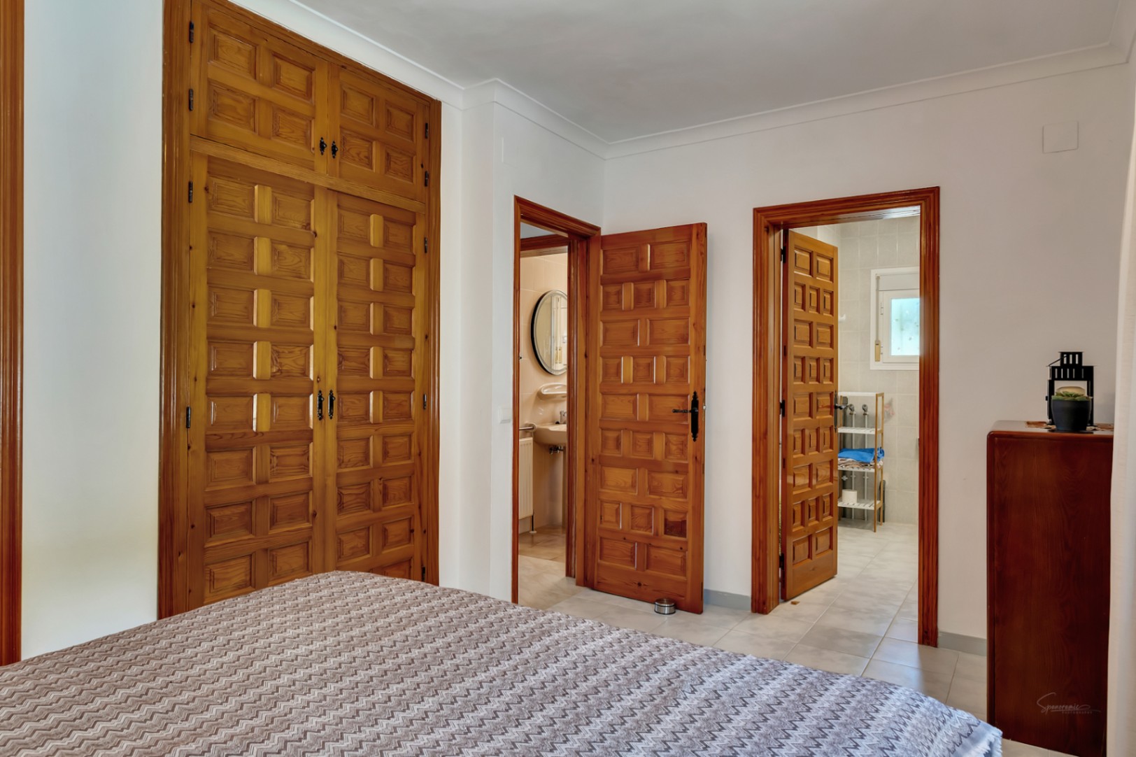 Chambre avec de grands placards intégrés en bois sculpté et deux accès vers des salles de bains privatives, mettant en valeur une menuiserie artisanale.