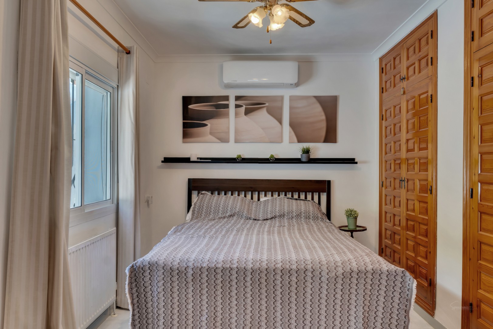 Chambre avec placards intégrés en bois sculpté, climatisation, radiateur et fenêtre à double vitrage avec rideaux neutres.