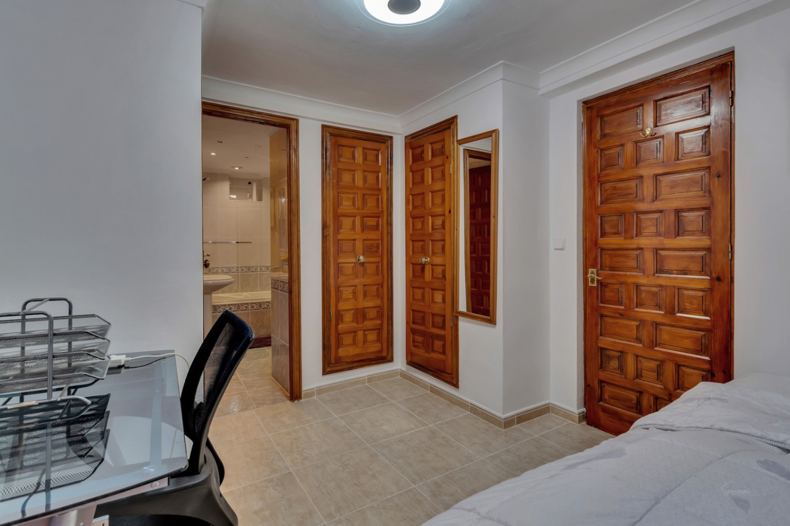 Chambre avec placards intégrés en bois sculpté, sol en grès cérame et accès à une salle de bain attenante équipée d'une baignoire et de carrelage clair.