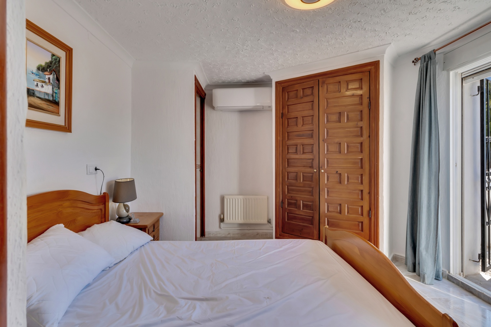 Chambre lumineuse avec lit en bois, armoire encastrée sculptée, climatisation et accès direct à la terrasse par de grandes baies vitrées coulissantes.