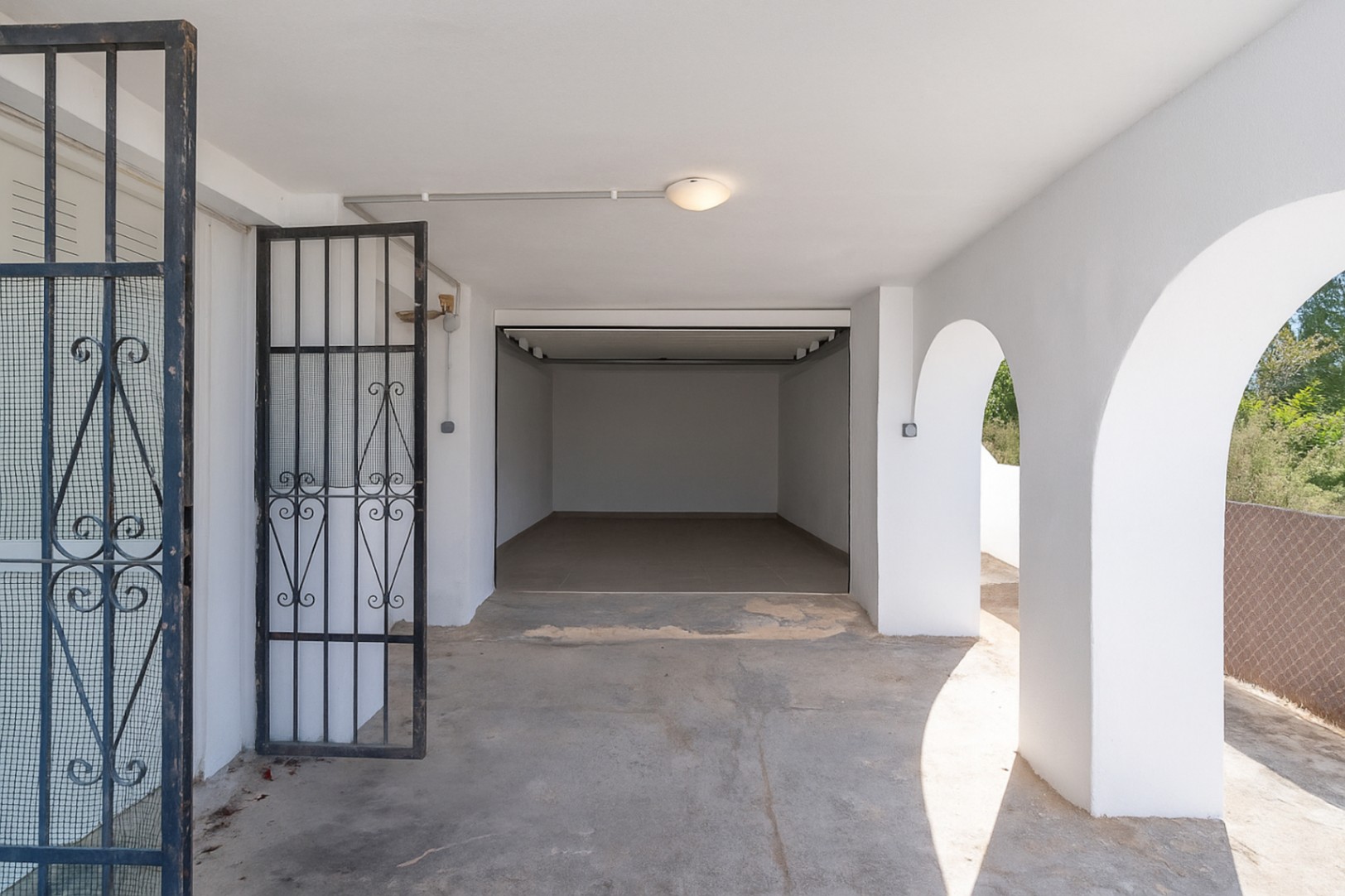 Garage fermé et espace de stationnement couvert avec arches méditerranéennes, murs blancs et grille de sécurité en fer forgé noir.