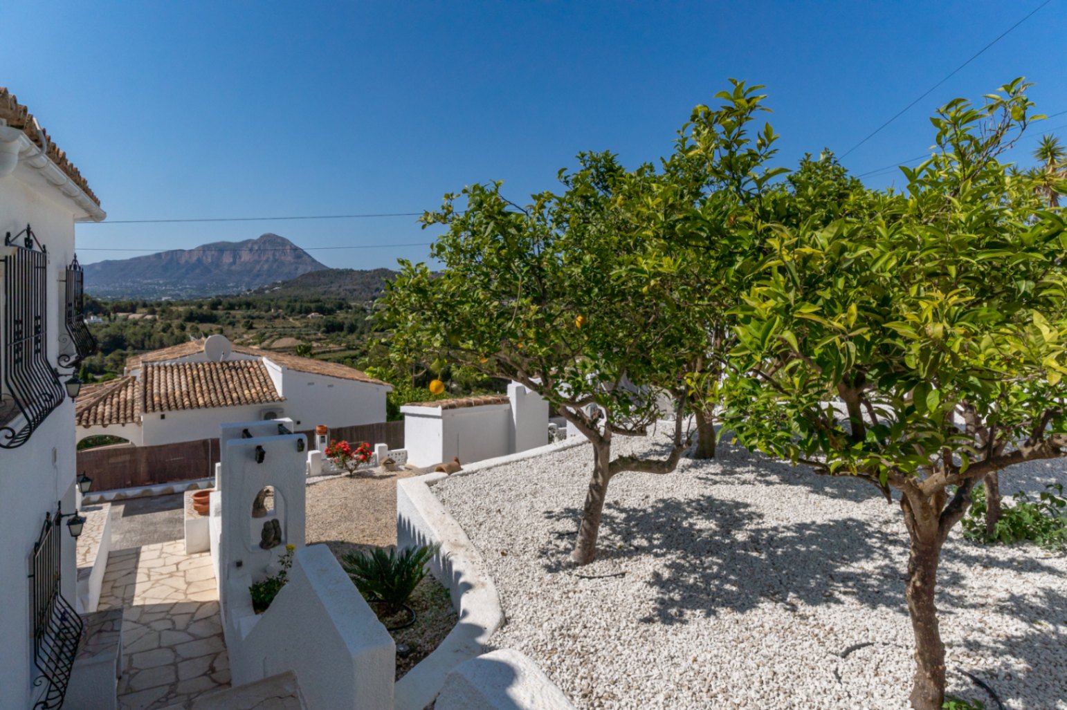 Jardin méditerranéen avec gravier blanc et agrumes, offrant une vue dégagée sur le mont Montgó depuis les terrasses extérieures de la propriété.