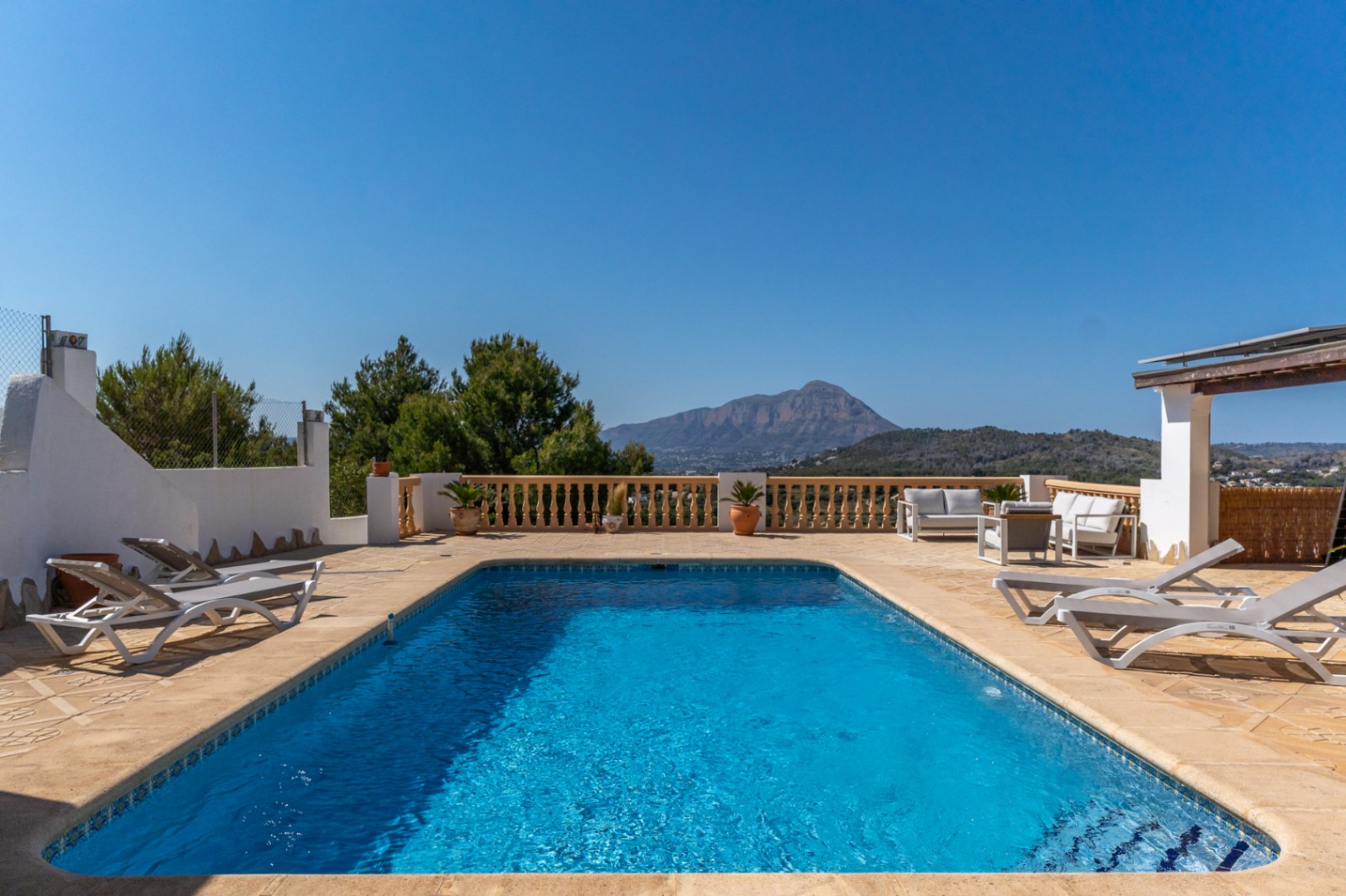 Piscine rectangulaire entourée d'une vaste terrasse en pierre avec transats, coin salon et vue imprenable sur le mont Montgó.