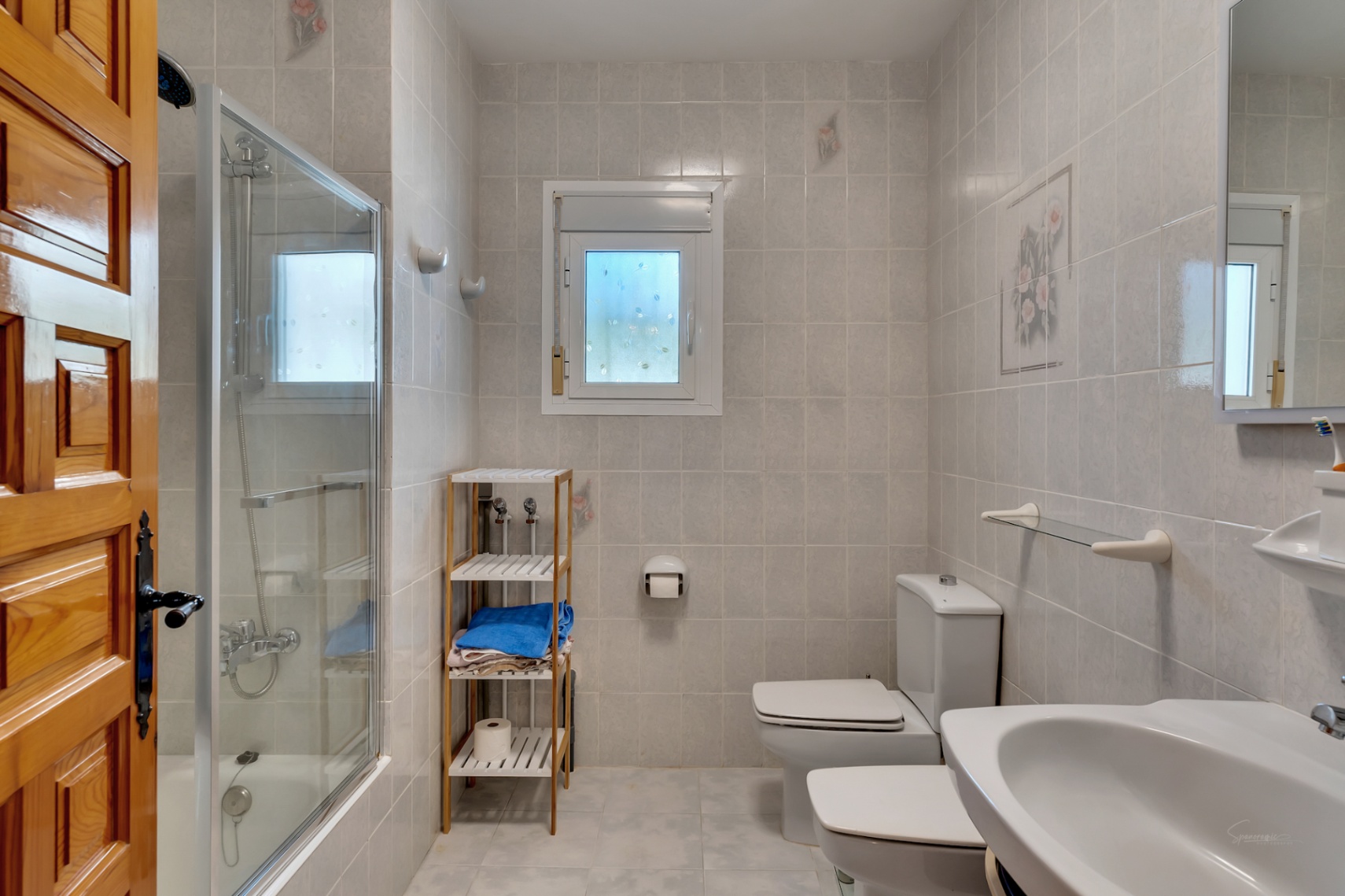 Salle de bain fonctionnelle avec douche vitrée, sanitaires blancs et murs carrelés. Elle dispose d'une fenêtre de lumière naturelle et d'une porte en bois massif.