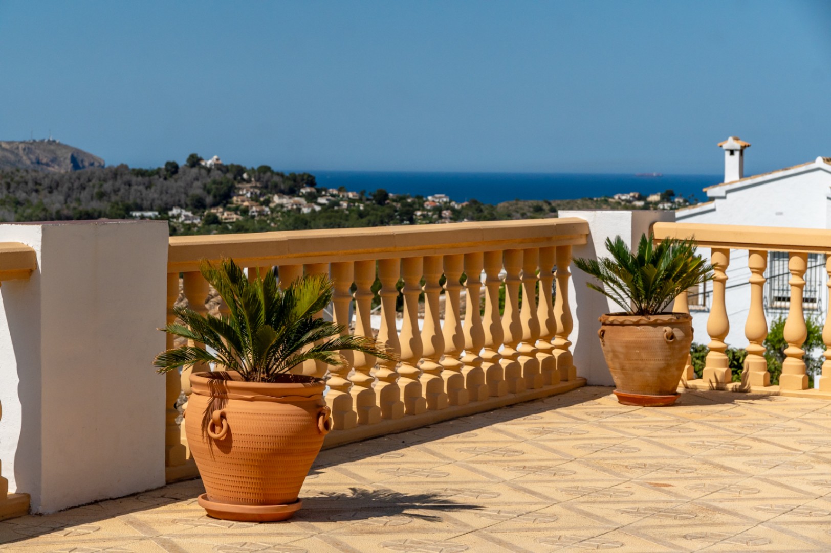 Terrasse surélevée avec sol en céramique à motifs, balustrade classique et jardinières en terre cuite offrant une vue panoramique sur la mer Méditerranée.