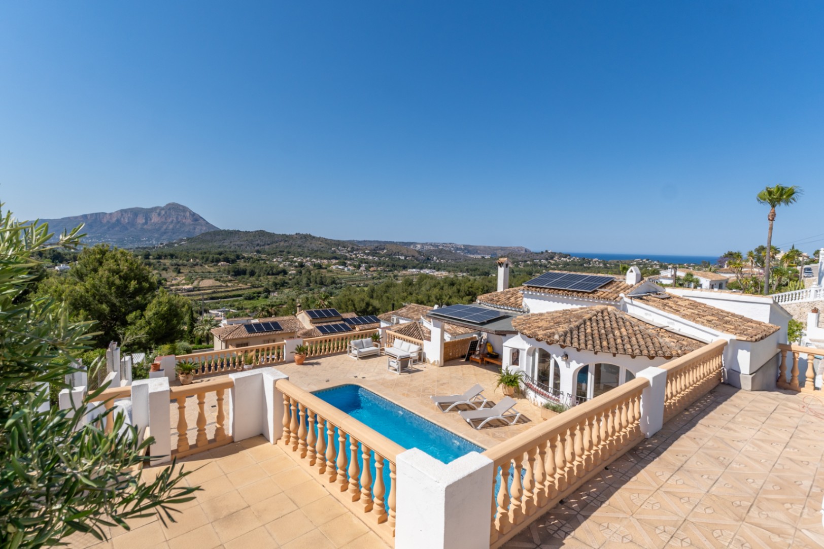 Vue panoramique depuis la terrasse supérieure montrant la piscine, les panneaux solaires et la vue dégagée sur le Montgó et la mer Méditerranée.