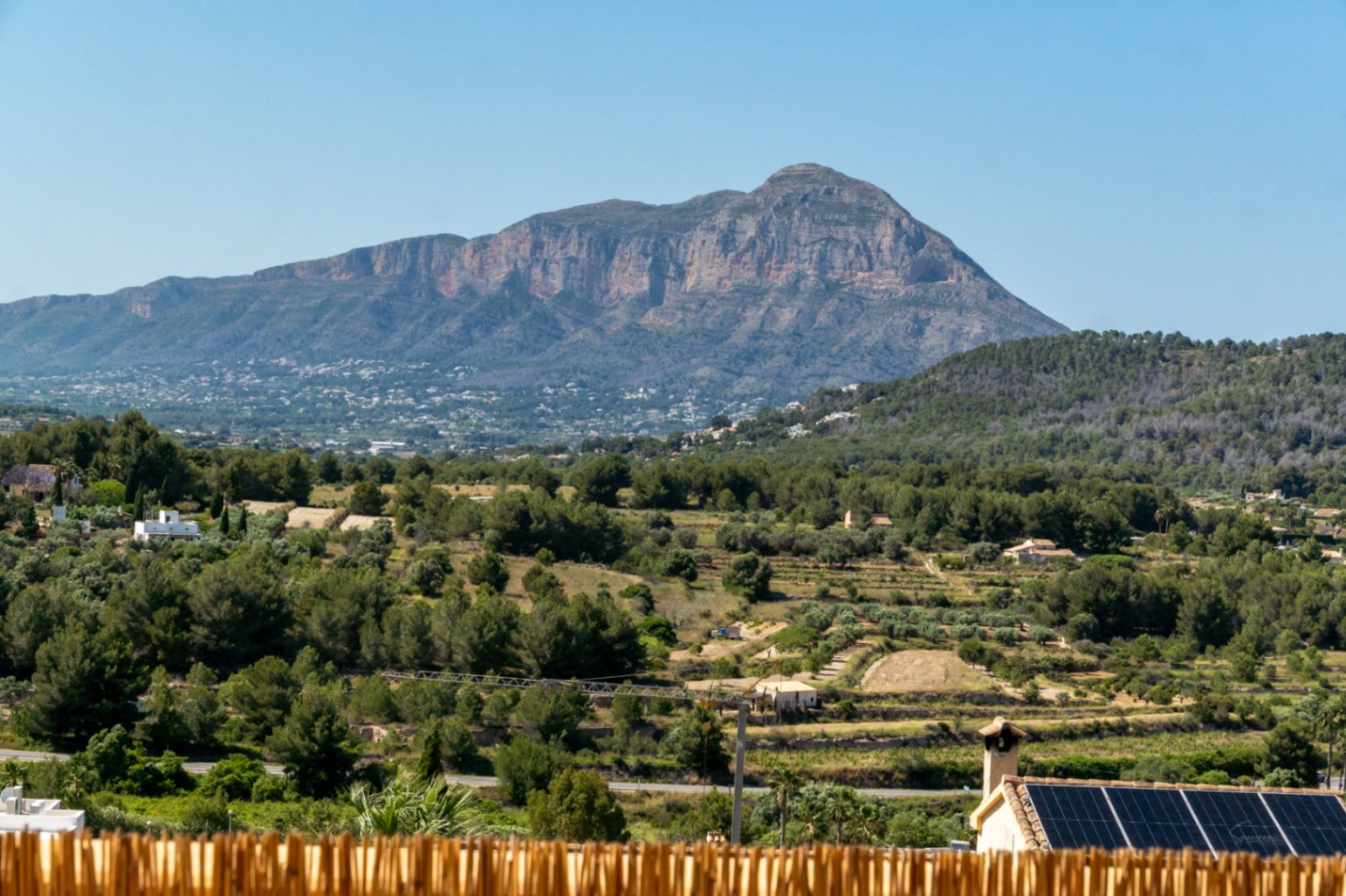 Vue panoramique sur le massif du Montgó et la vallée méditerranéenne, avec un toit équipé de panneaux solaires photovoltaïques au premier plan.