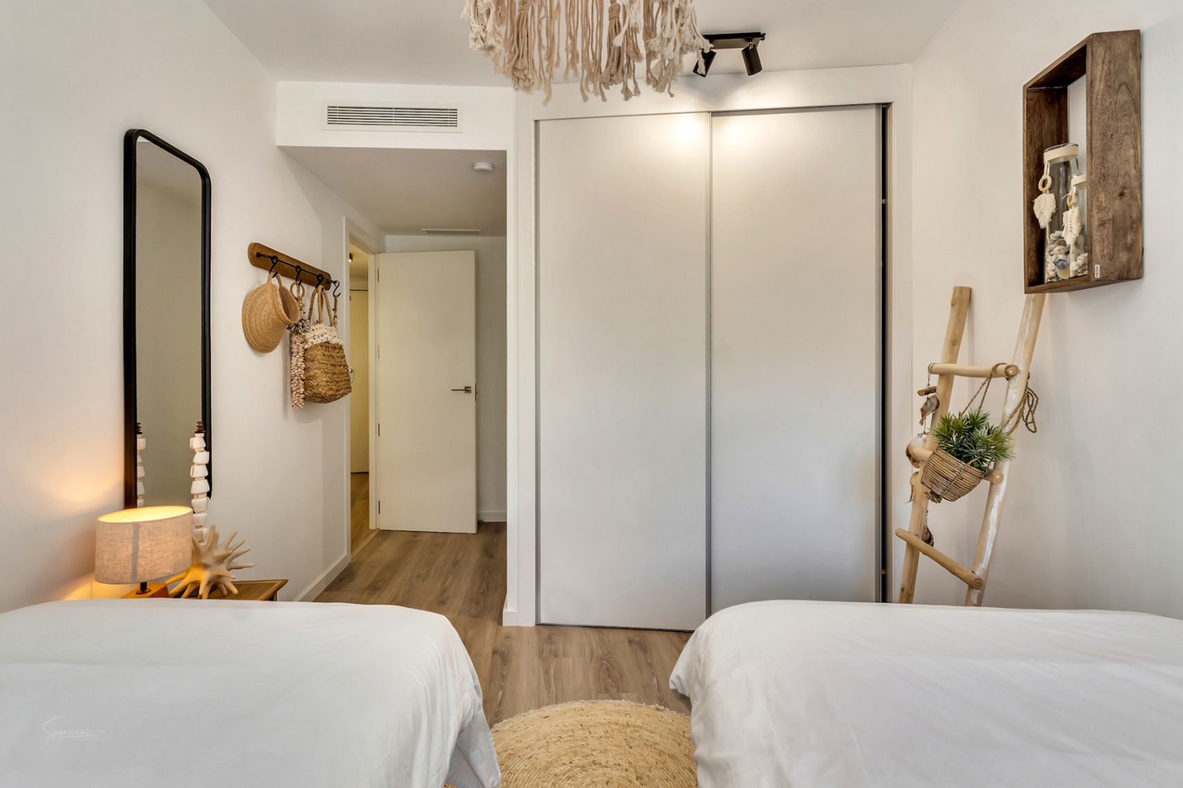 Chambre avec lits jumeaux, grand placard intégré à portes coulissantes blanches et décoration d'inspiration méditerranéenne avec des touches de bois naturel.