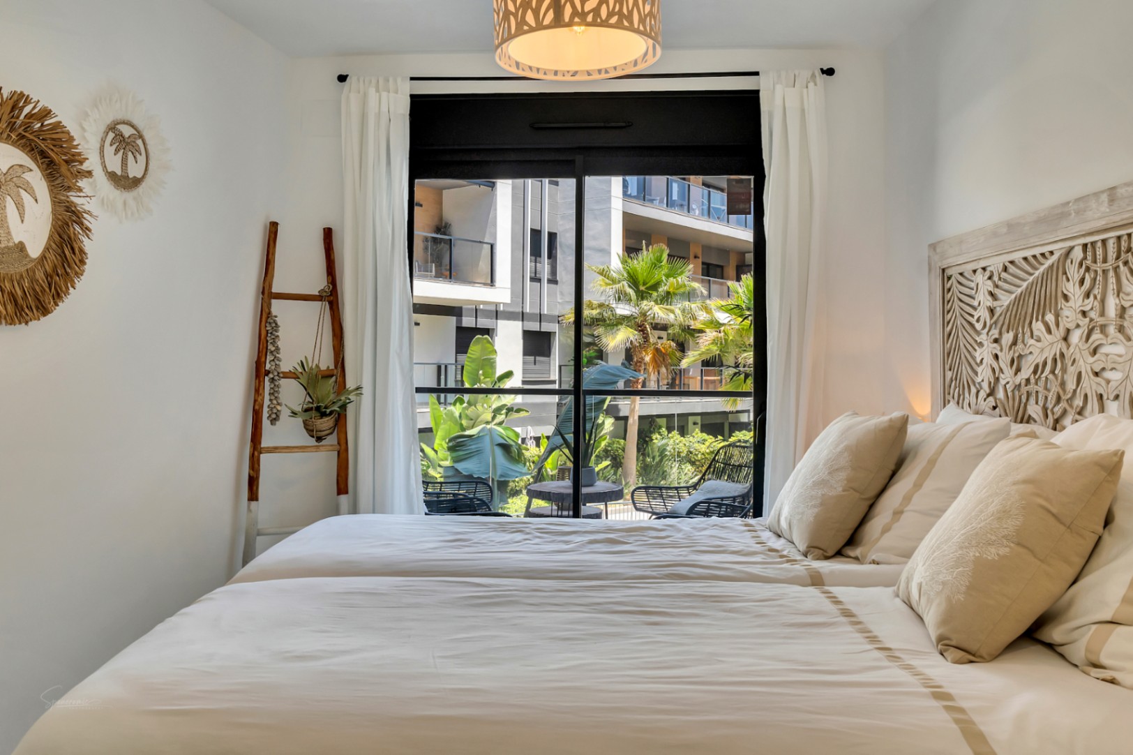Chambre lumineuse avec tête de lit en bois sculpté, décoration d'inspiration méditerranéenne et accès direct à une terrasse privée donnant sur les jardins.