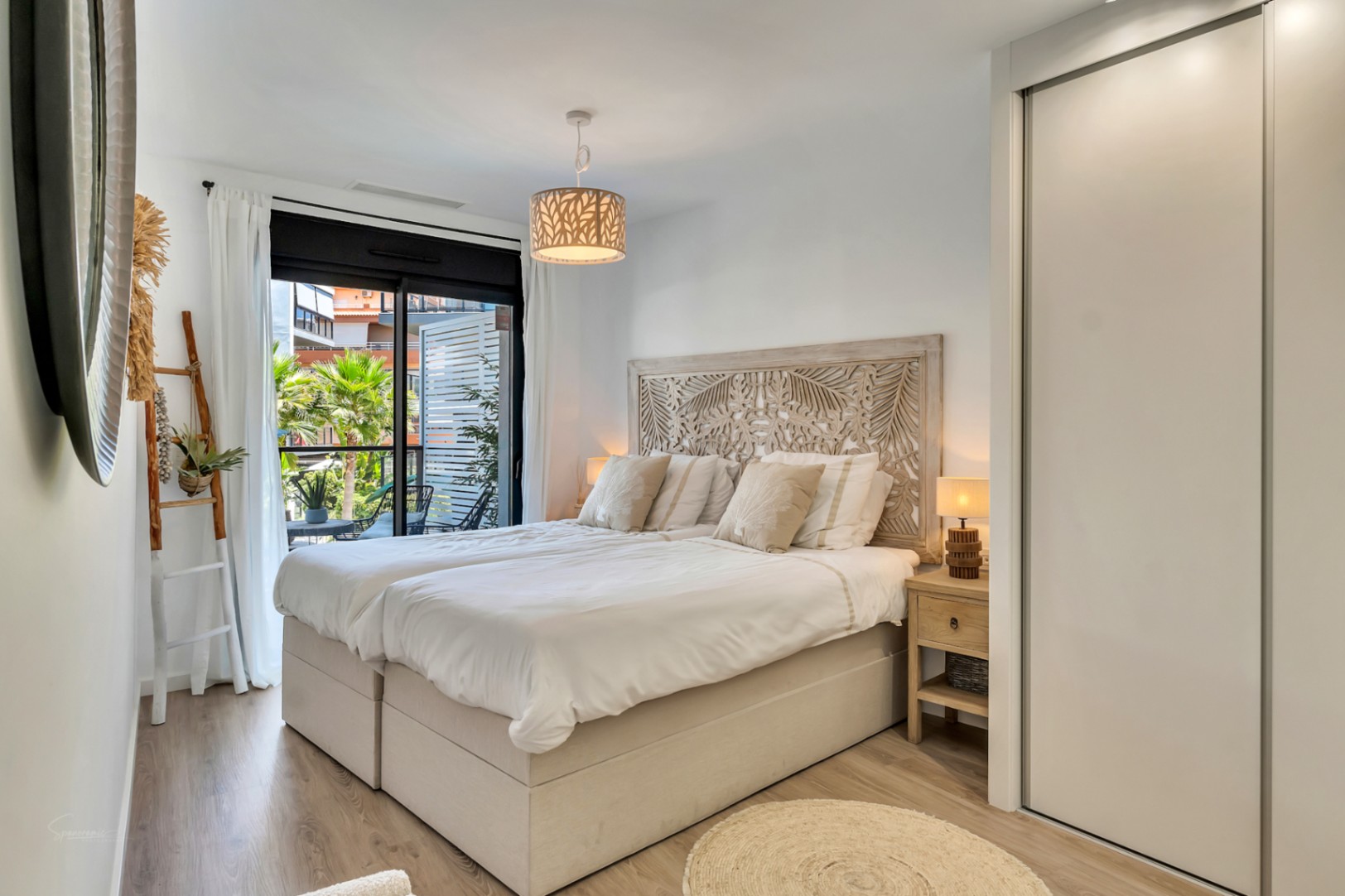 Chambre lumineuse avec tête de lit en bois sculpté, placards intégrés et accès direct à une terrasse privée offrant une vue sur le jardin.