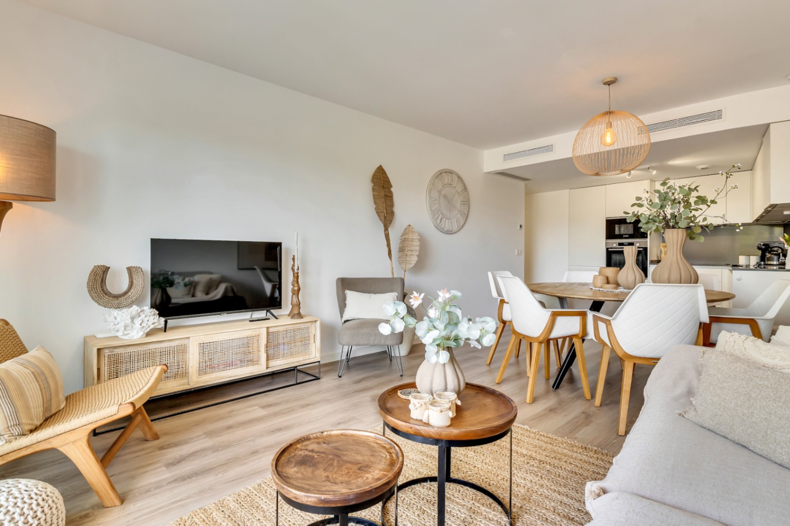Espace de vie ouvert comprenant un salon aux tons naturels, une salle à manger élégante et une cuisine moderne intégrée avec finitions blanches.