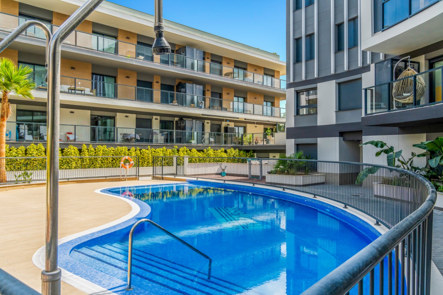 Piscine communautaire aux formes arrondies entourée d'une terrasse en carrelage et de bâtiments résidentiels modernes aux façades contemporaines.