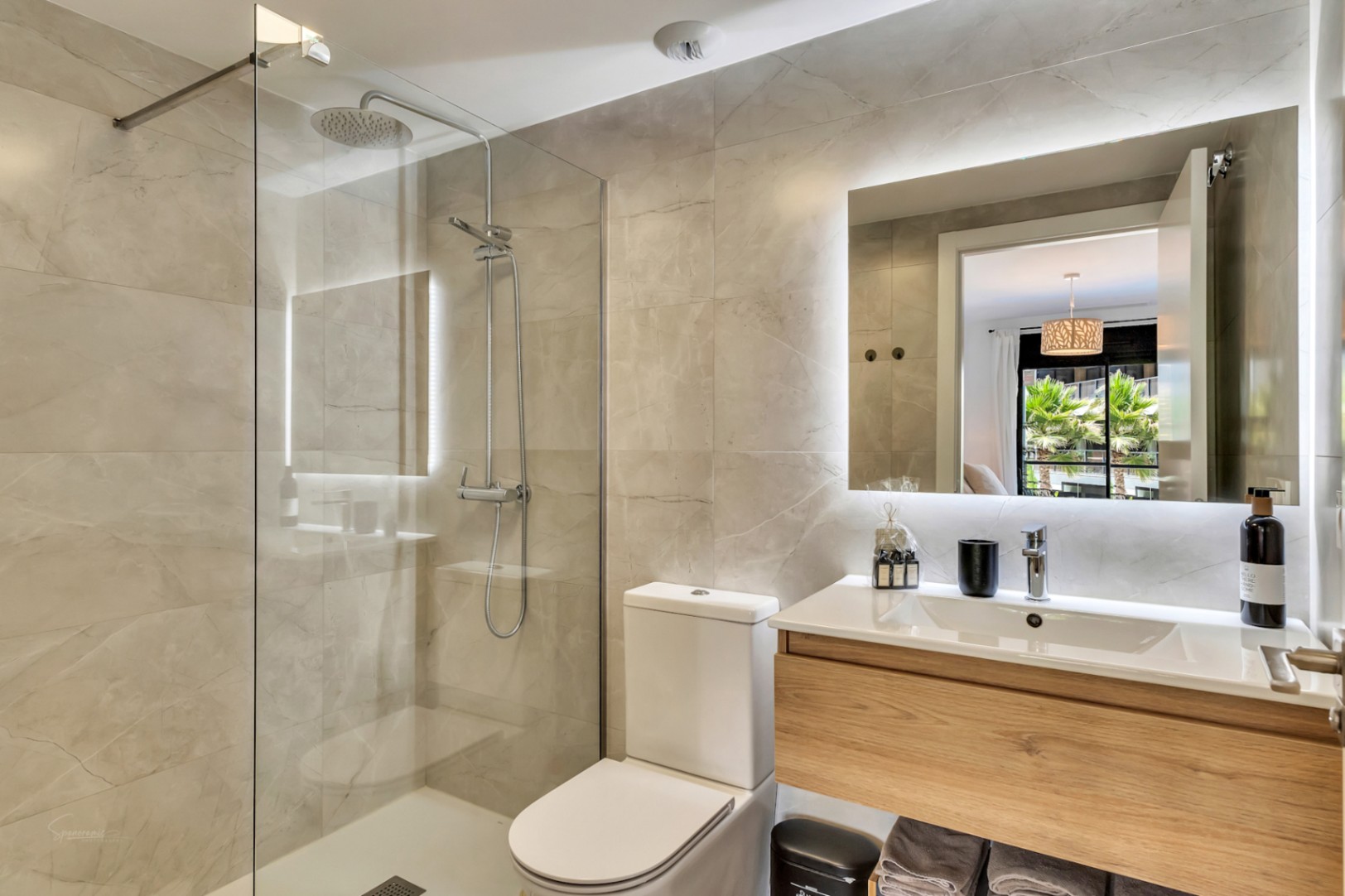 Salle de bain moderne avec douche à l'italienne, paroi en verre et carrelage effet marbre. Elle dispose d'un meuble vasque suspendu en bois et d'un miroir rétroéclairé par LED.