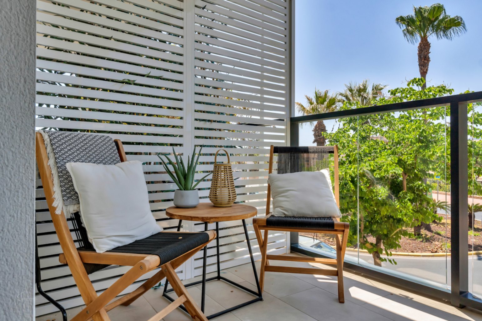 Terrasse privée avec persiennes blanches, mobilier en bois et garde-corps en verre offrant une vue dégagée sur la végétation méditerranéenne environnante.