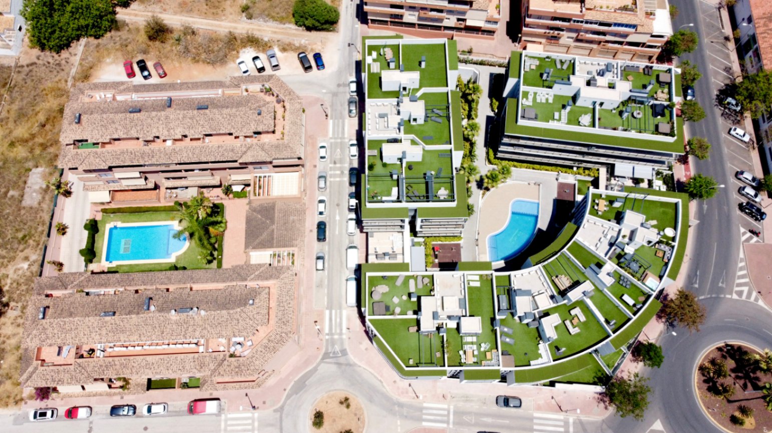 Vue aérienne du complexe résidentiel contemporain à Jávea, mettant en valeur son architecture courbe, ses vastes toits-terrasses en gazon synthétique et sa piscine commune.