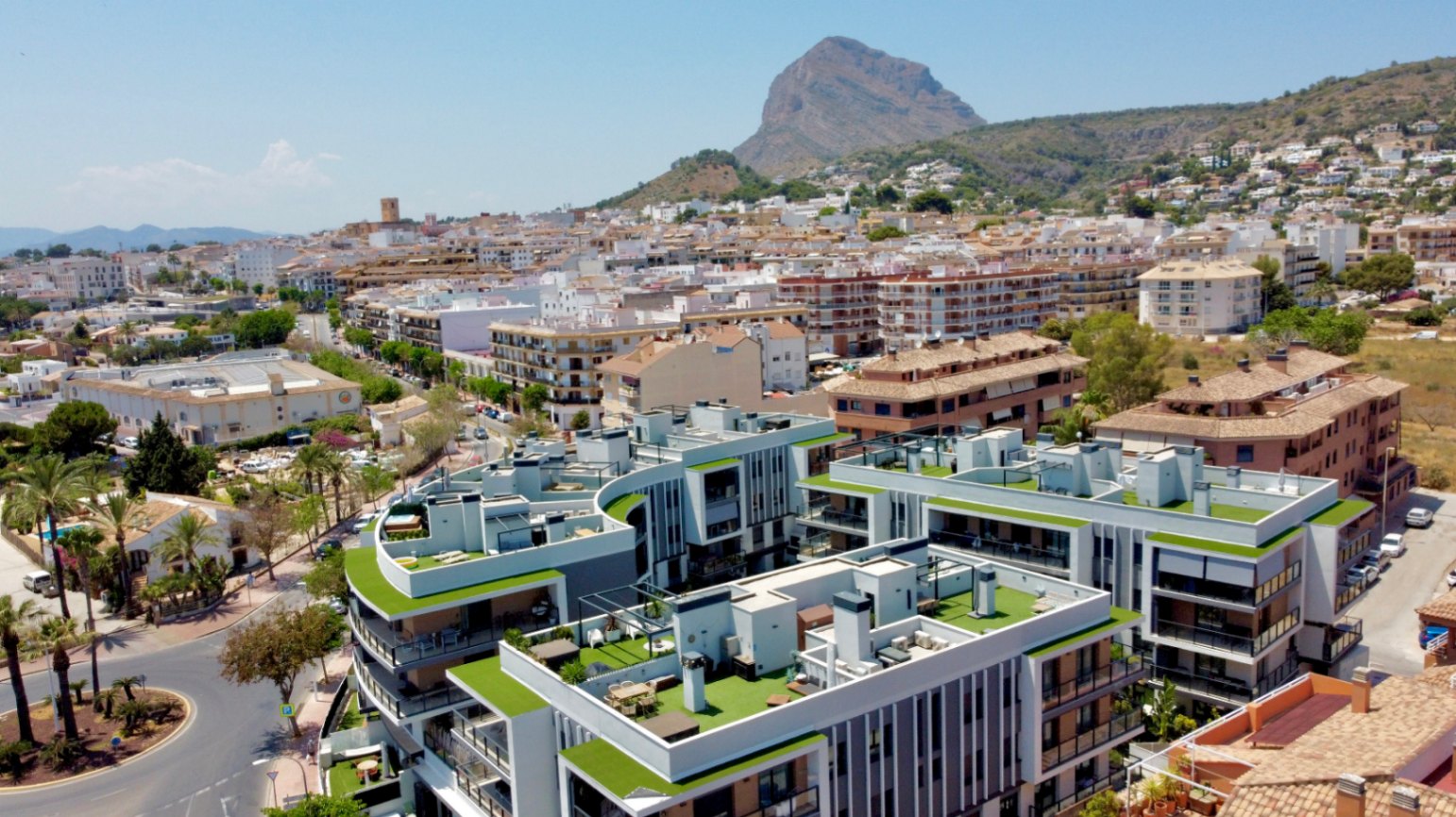 Vue aérienne du complexe résidentiel moderne à Jávea, avec ses toits-terrasses végétalisés et une vue imprenable sur le Montgó et la vieille ville.