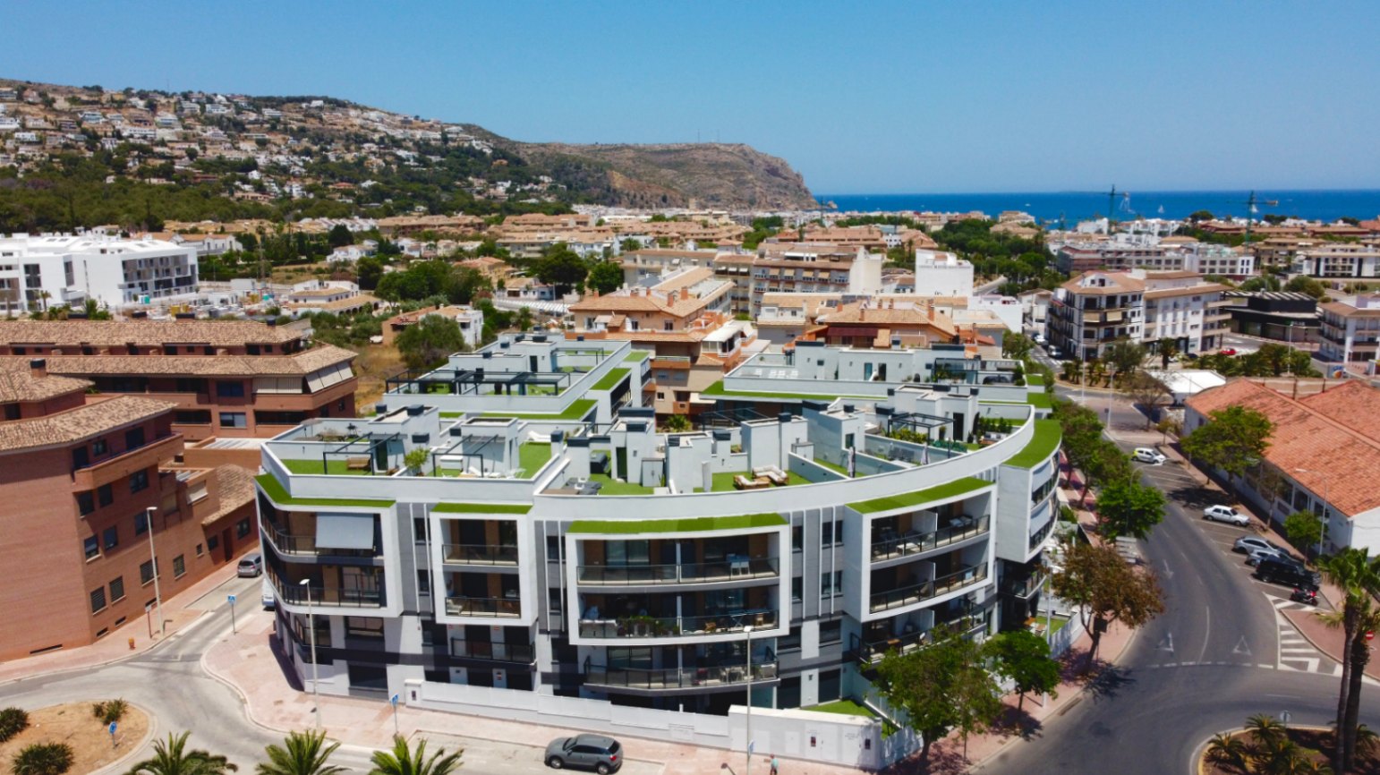 Vue aérienne du complexe résidentiel moderne à l'architecture courbe, mettant en avant les terrasses de toit privées et la proximité de la mer Méditerranée à Jávea.