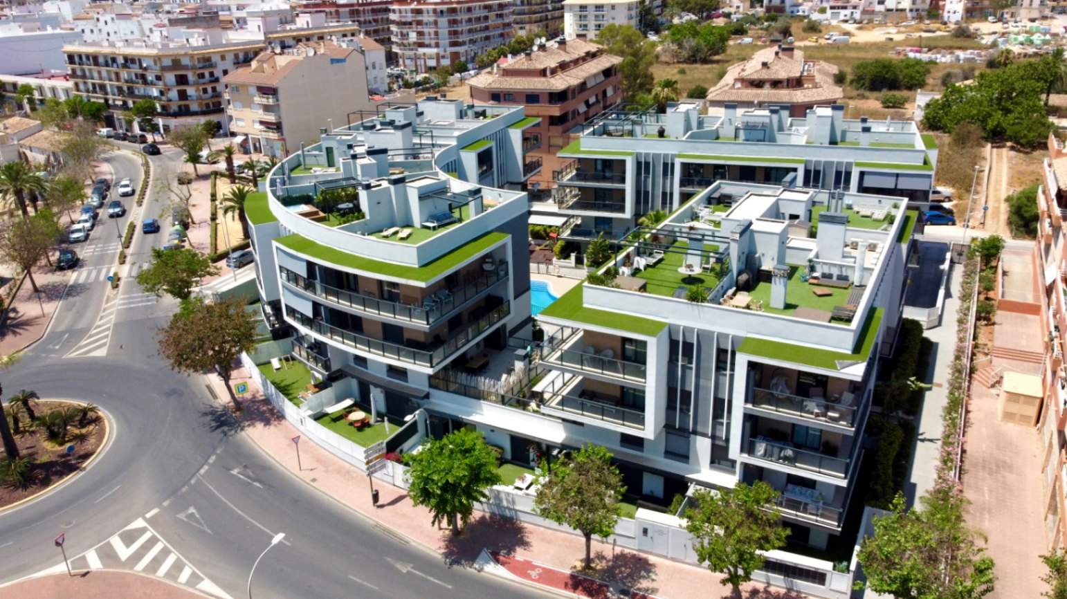 Vue aérienne du complexe résidentiel moderne avec architecture courbe, toits-terrasses végétalisés et piscine centrale au cœur d'un quartier urbain dynamique.