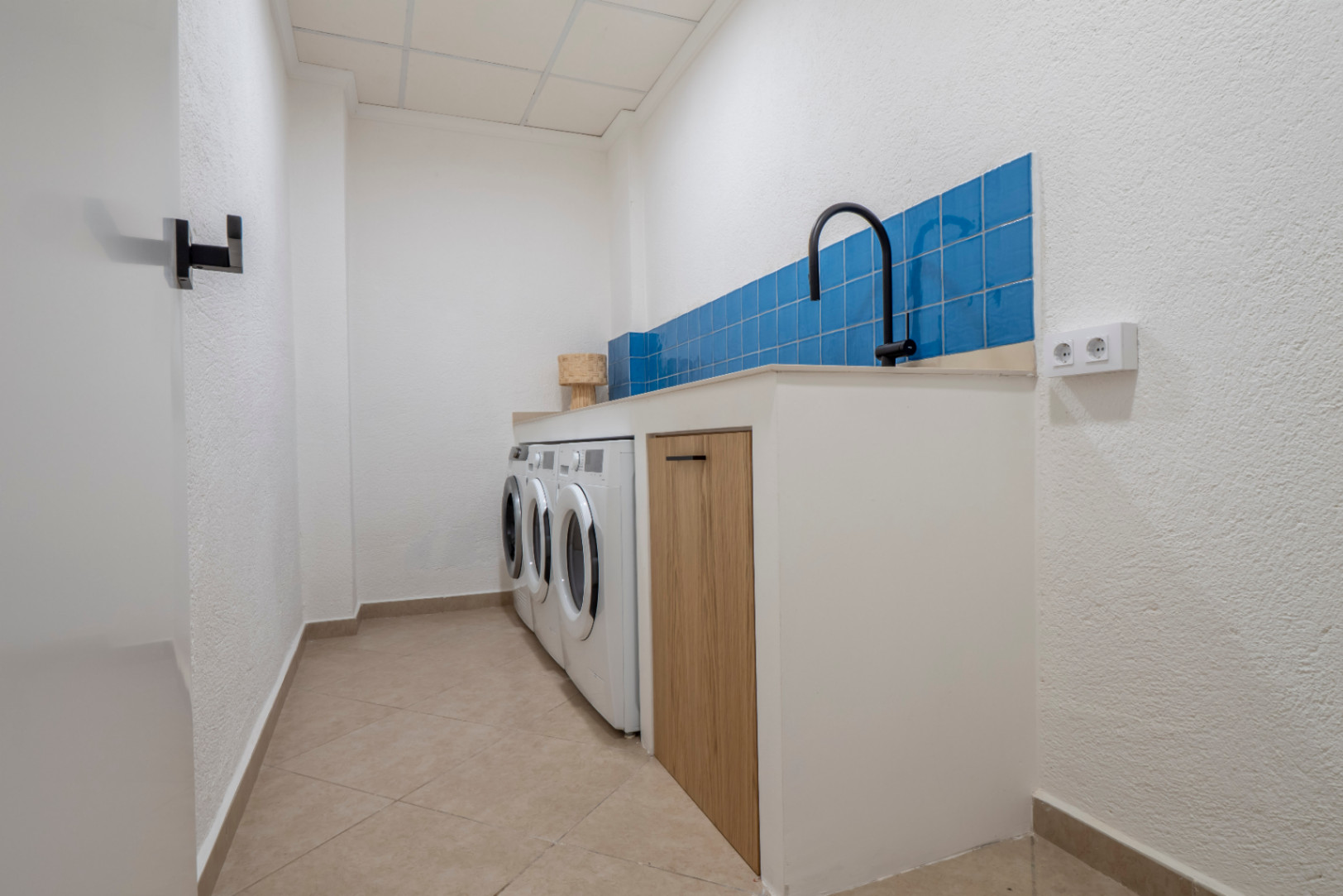 Buanderie fonctionnelle avec carrelage bleu, machines à laver et plan de travail en bois clair.