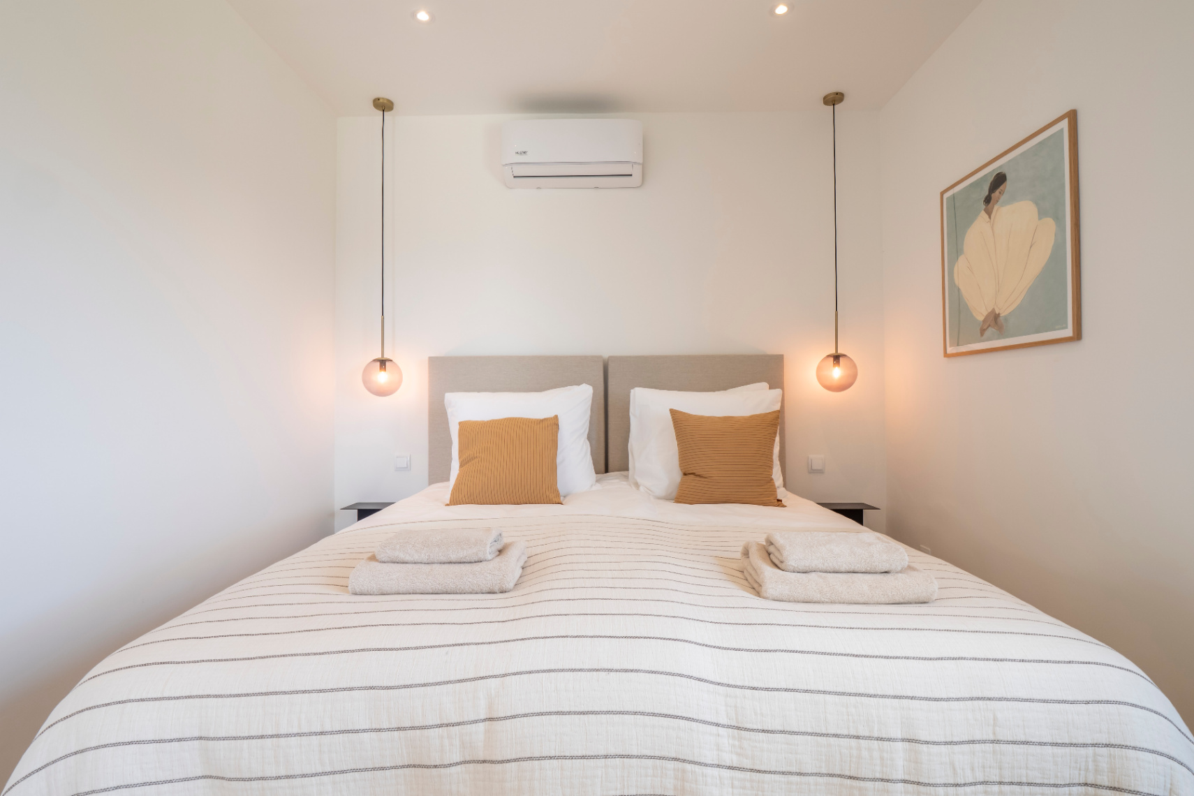 Chambre avec lit double, linge de lit rayé et suspensions sphériques.