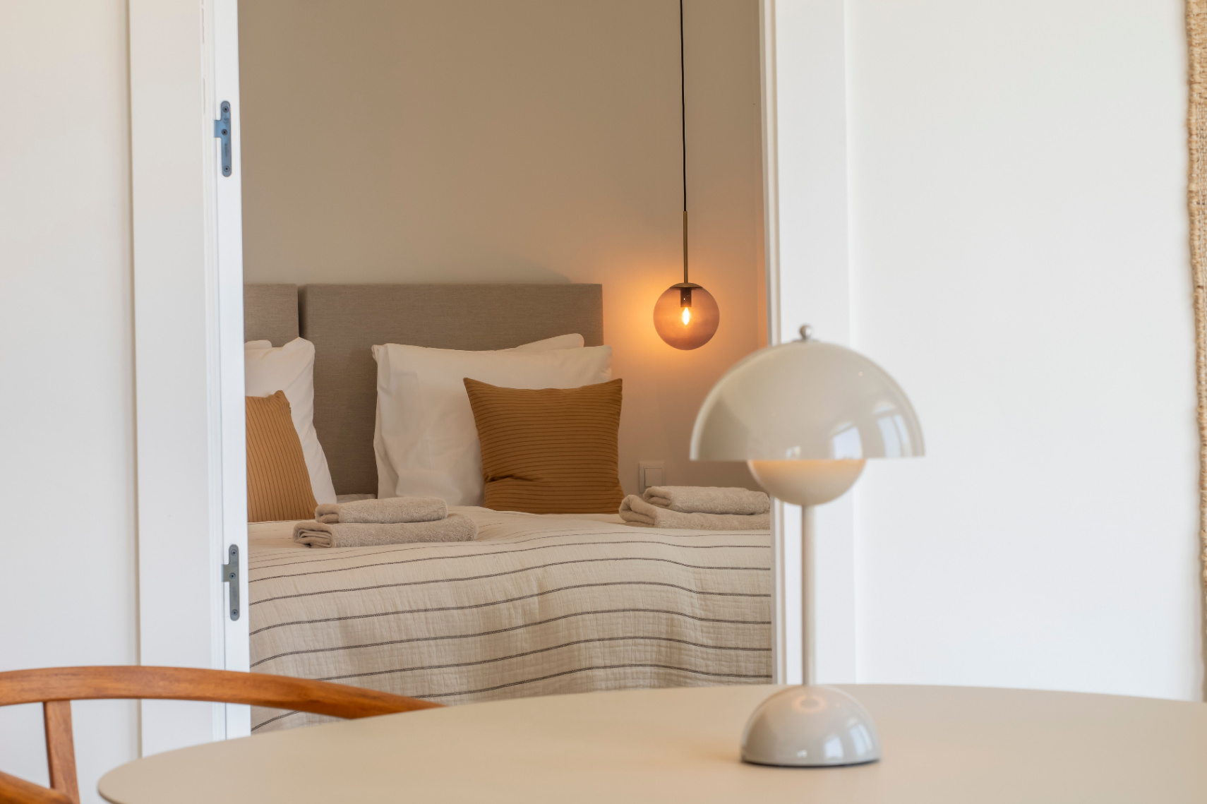 Chambre avec lit double, suspension sphérique et linge de lit rayé. Table ronde avec lampe de chevet champignon.