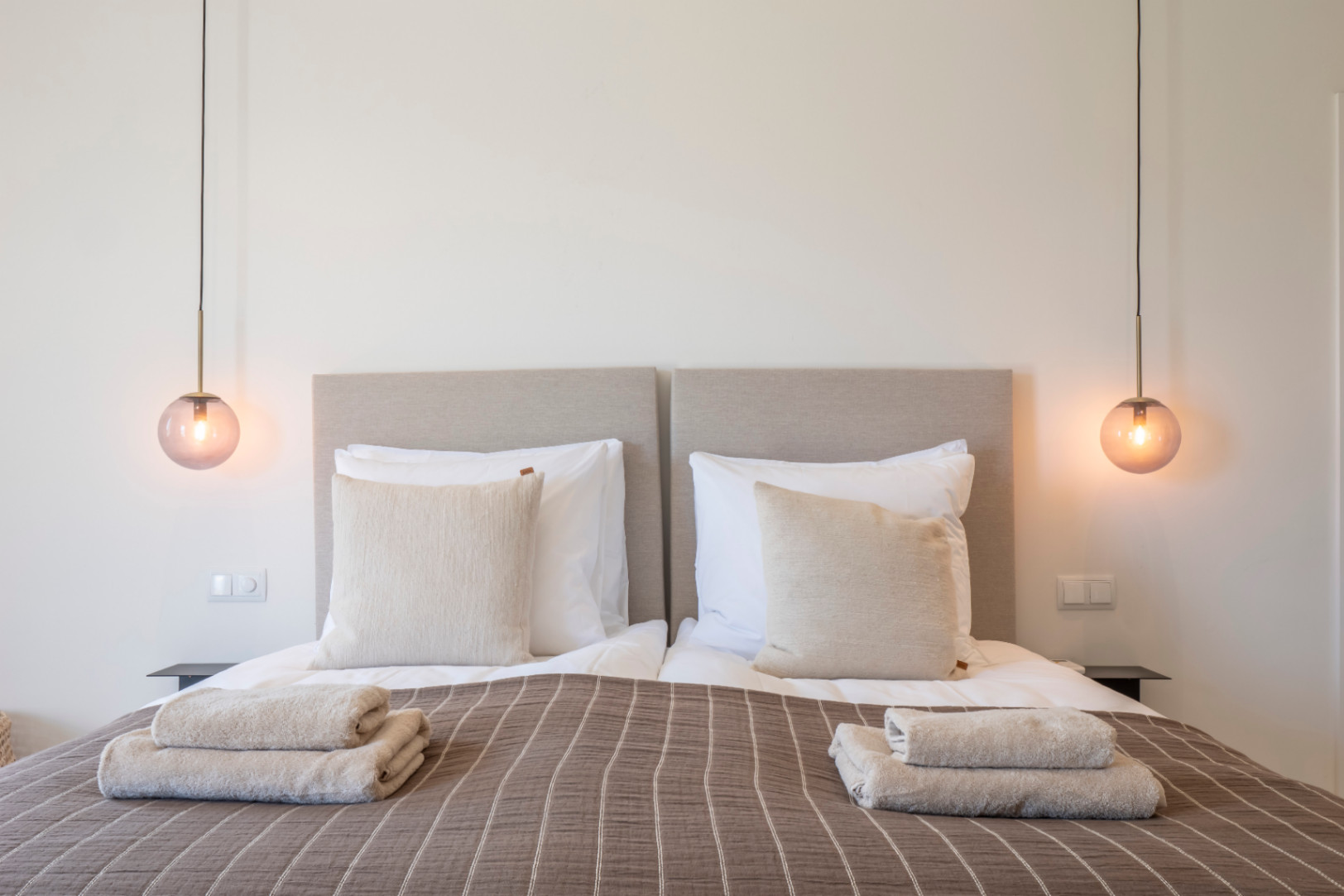 Chambre avec lits jumeaux, têtes de lit rembourrées et suspensions en verre ambré.