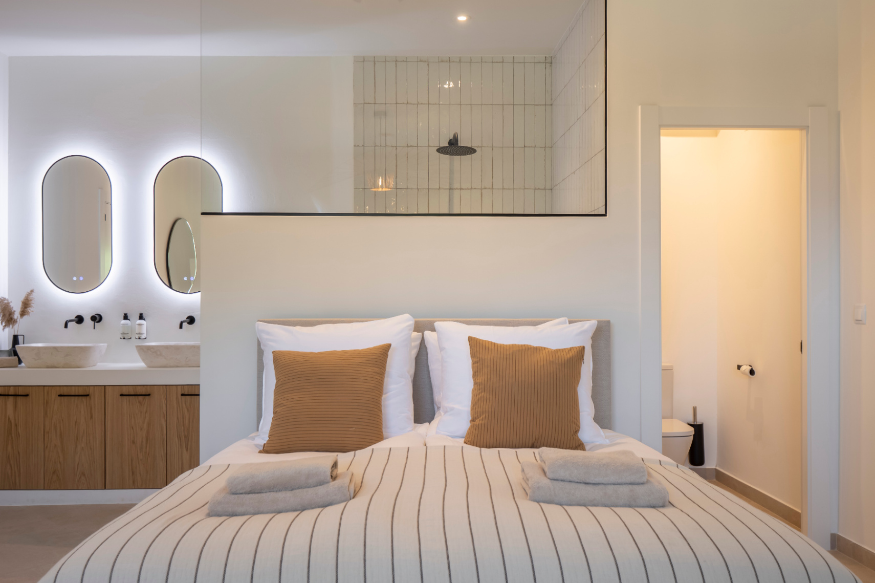 Chambre avec salle de bain attenante. Vasques en pierre sur meuble en bois clair et éclairage LED.