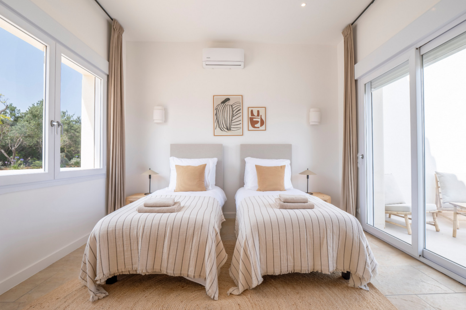 Chambre lumineuse avec lits jumeaux, linge de lit rayé et décor minimaliste. Accès à une terrasse extérieure.