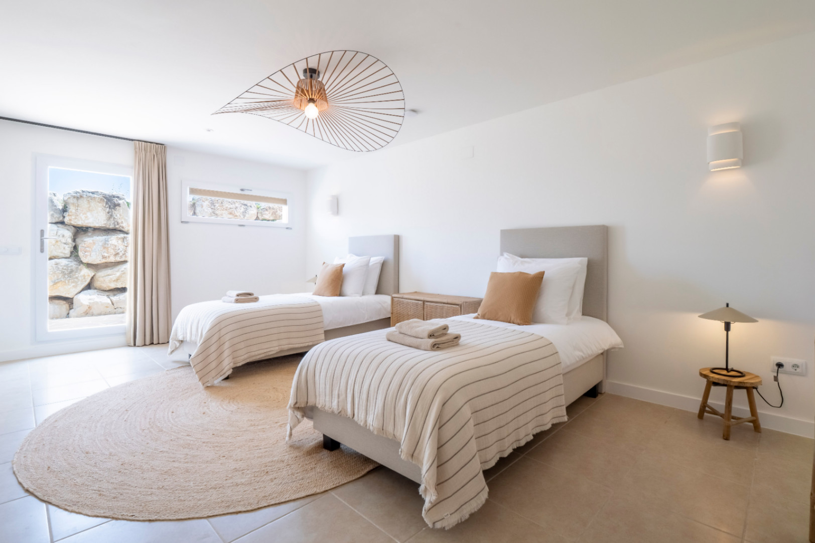 Chambre lumineuse avec lits jumeaux, tapis en jute et luminaire design.