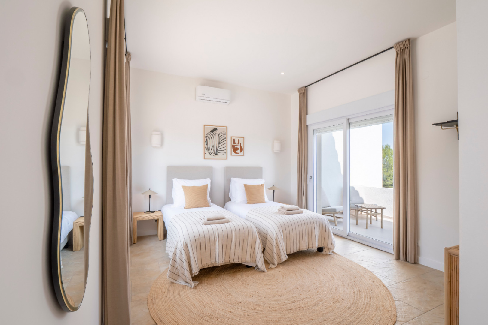 Chambre lumineuse avec lits jumeaux, tapis rond en jute et accès à une terrasse extérieure.