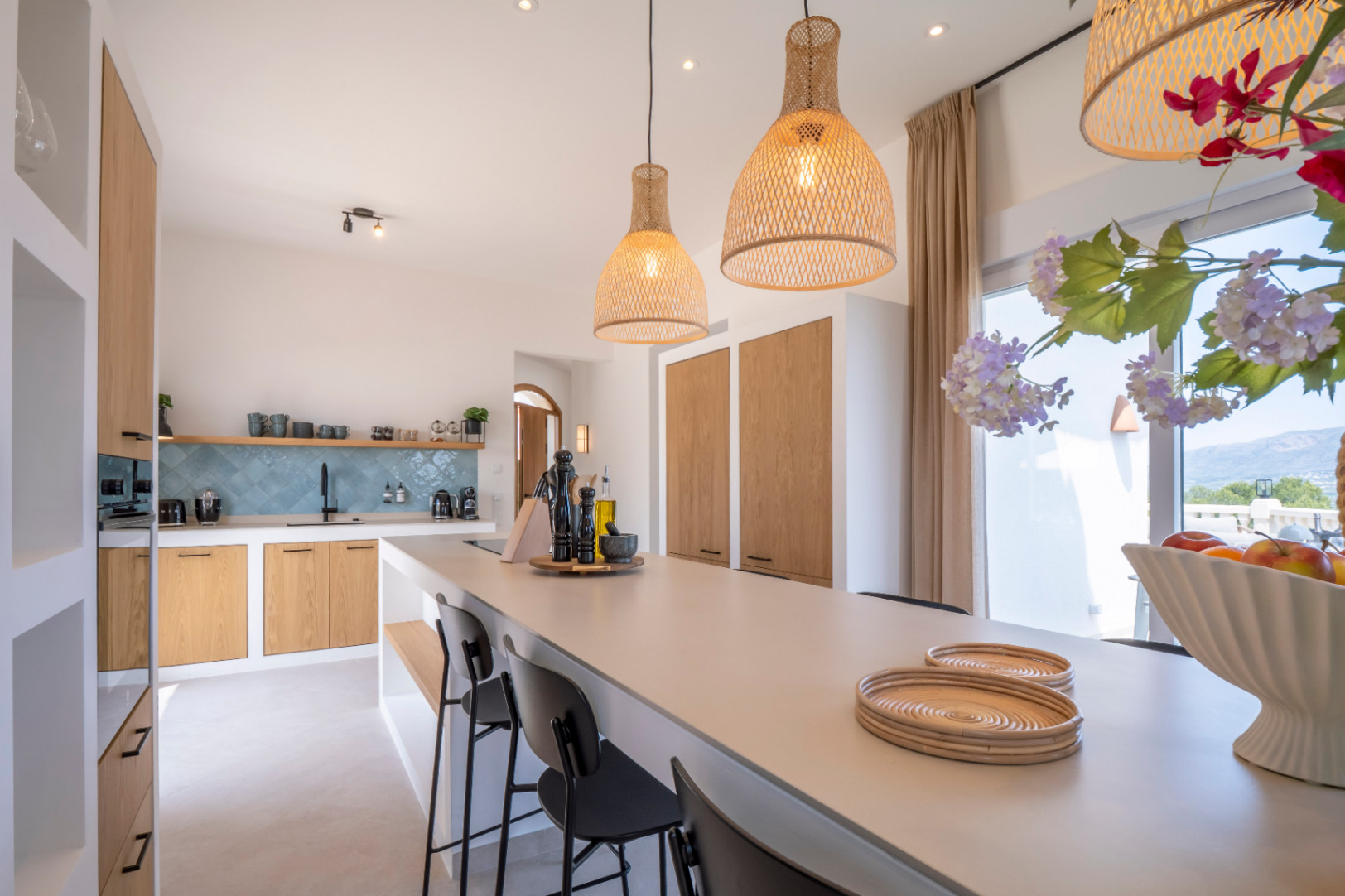 Cuisine lumineuse avec îlot central, lampes en osier et mobilier en bois clair. Faïence turquoise au mur.