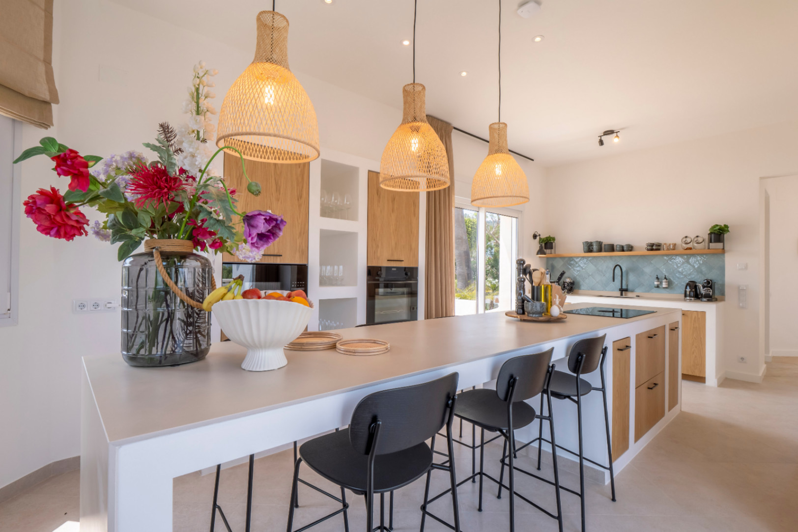 Cuisine moderne avec îlot central, tabourets noirs et suspensions en osier.