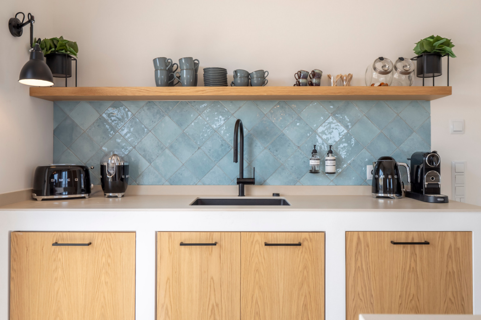 Détail de la cuisine avec évier, carreaux turquoise et appareils Smeg. Étagères en bois clair.