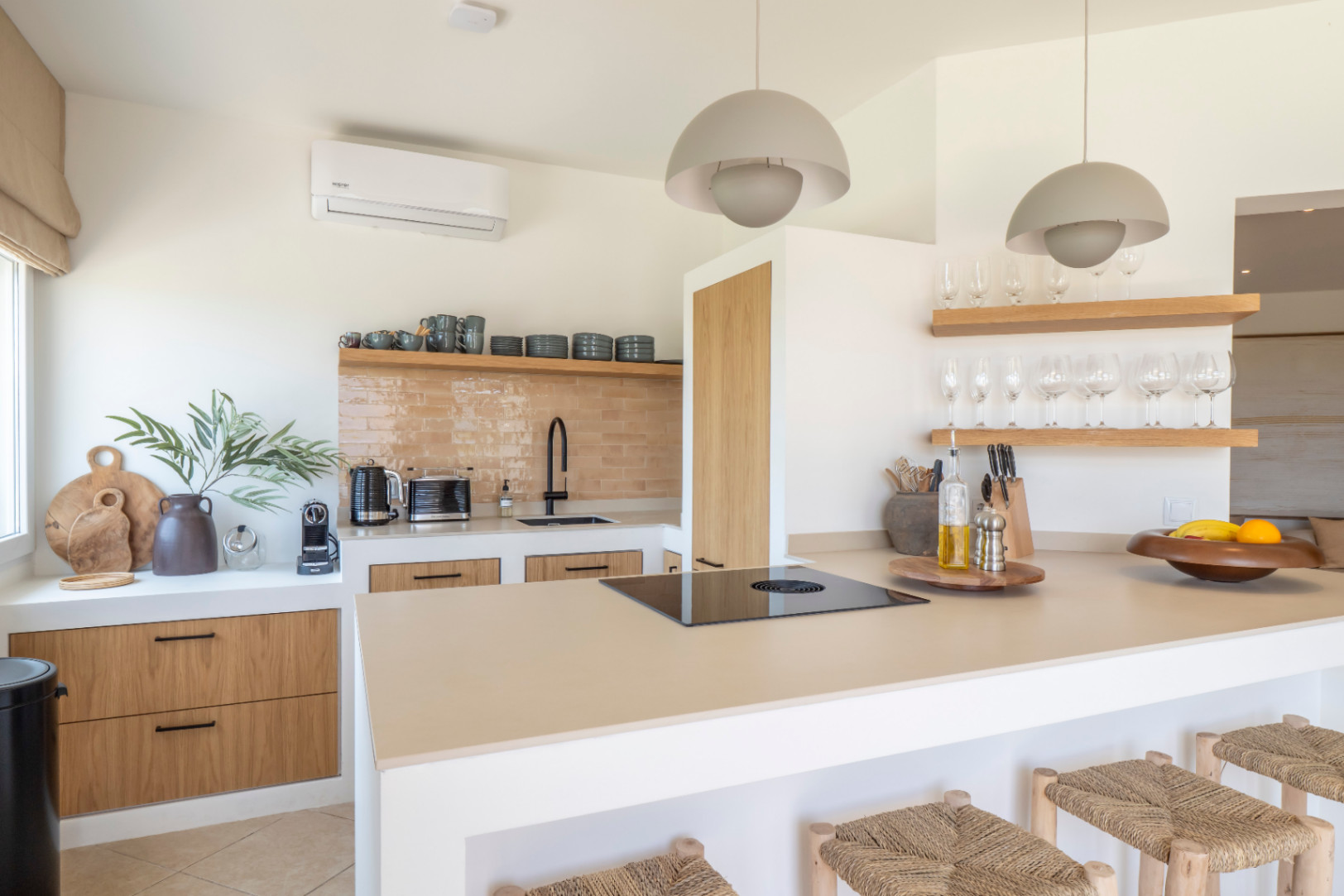 Détail de la cuisine avec îlot central, tabourets en bois et plan de travail clair. Étagères avec verrerie et vaisselle.