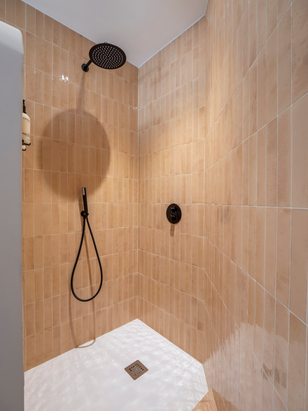 Détail de la douche avec des carreaux verticaux en terre cuite et robinetterie noire mate.