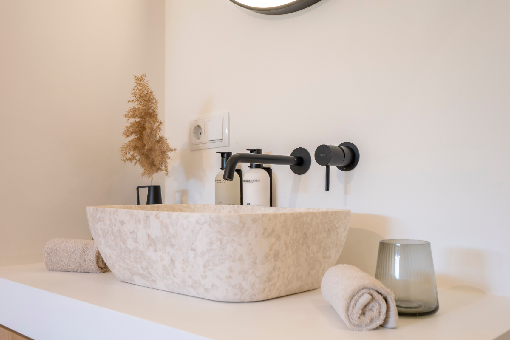 Détail de salle de bain avec lavabo en pierre naturelle et robinetterie noire mate. Décor minimaliste et serviettes assorties.