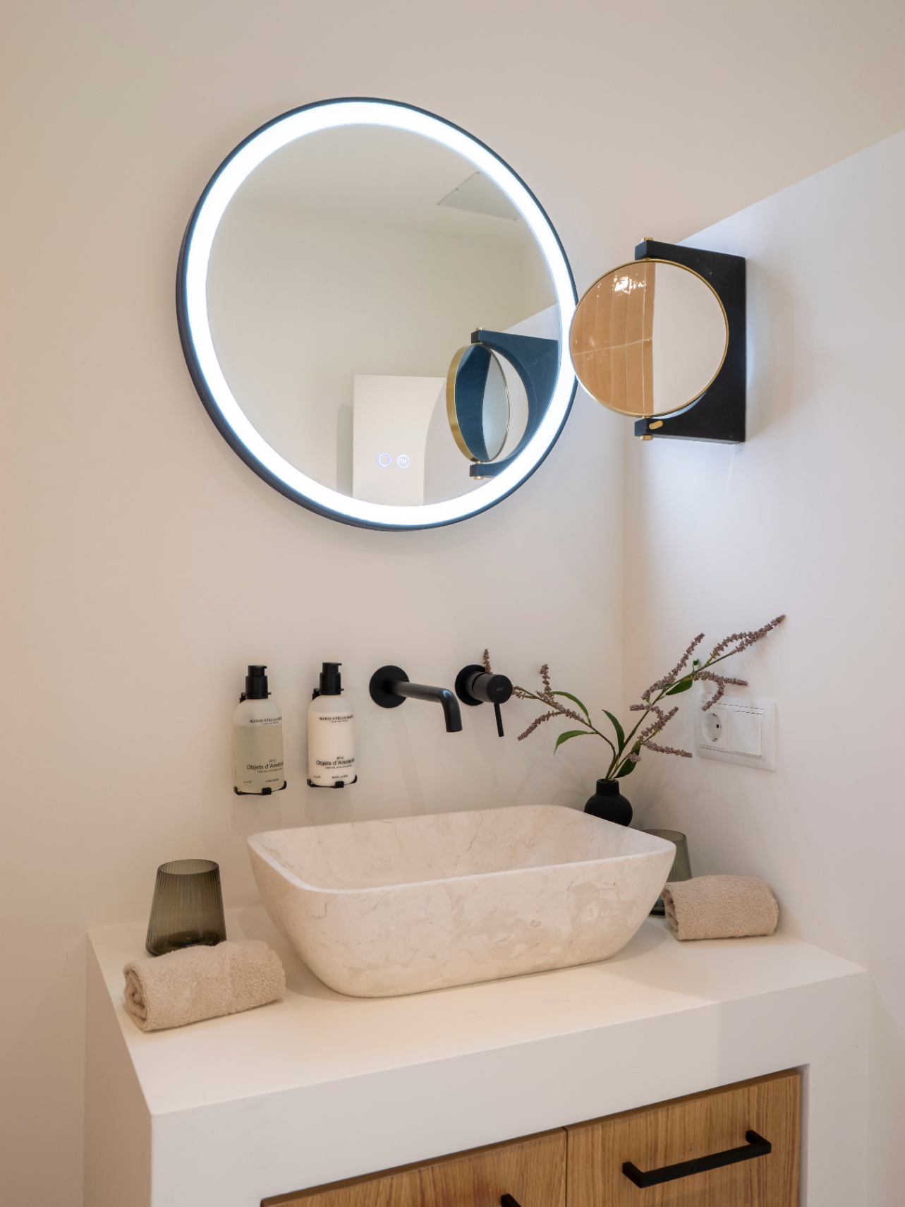 Détail de salle de bain avec vasque en pierre, robinetterie noire mate et miroir à éclairage LED.