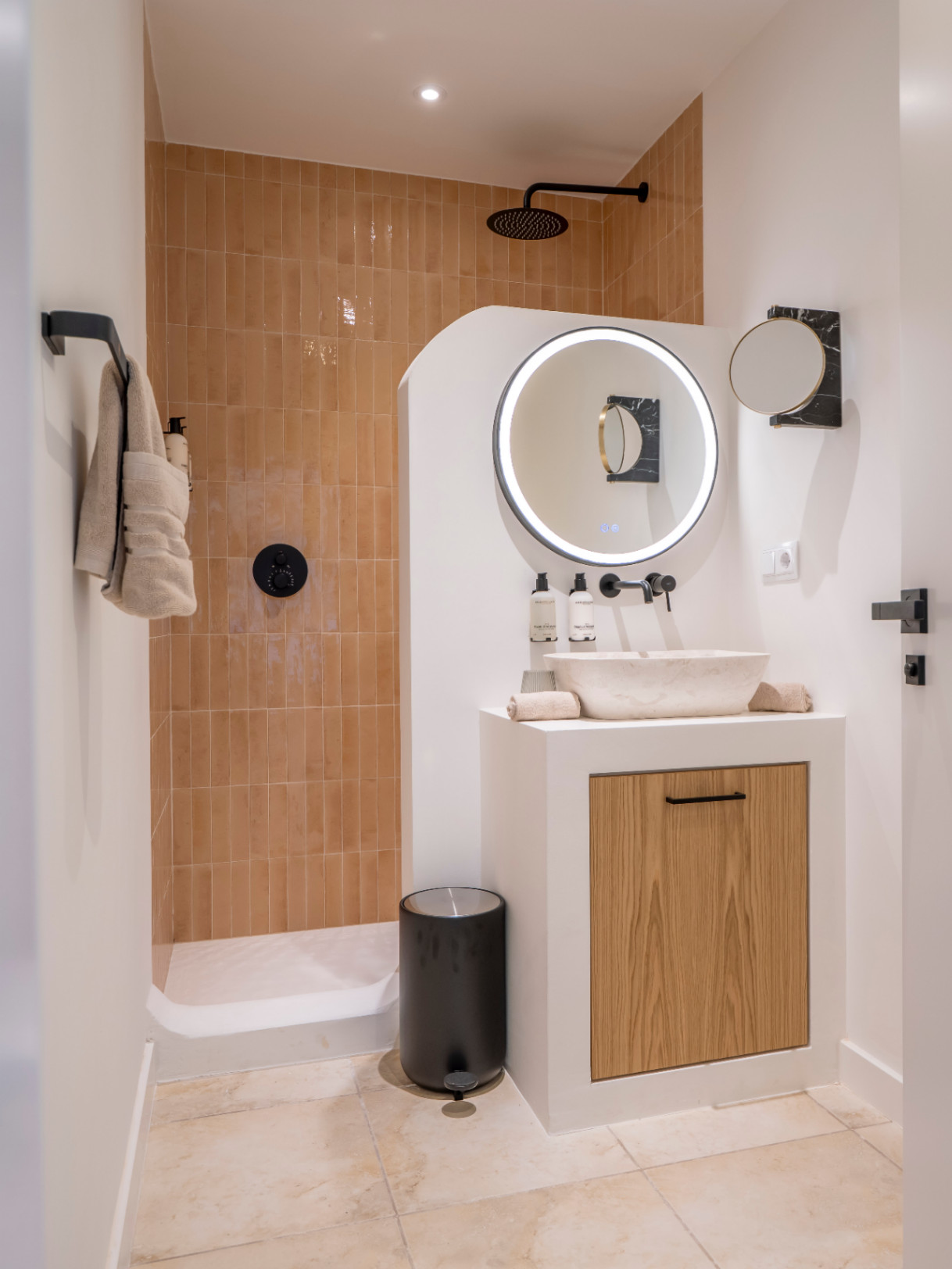 Détail d'une salle de bain moderne avec douche à l'italienne et vasque en pierre sur meuble en bois clair.